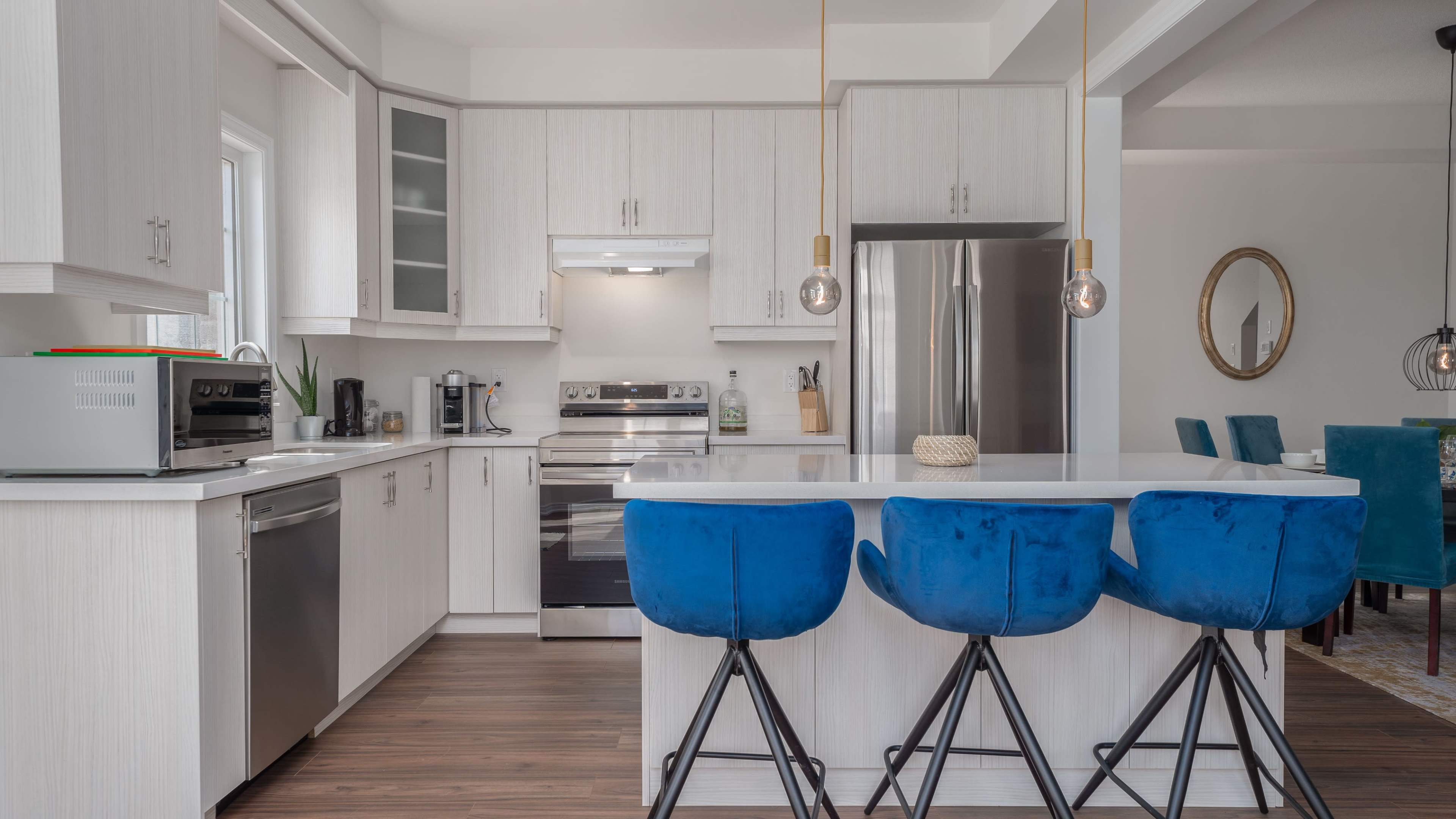 The kitchen features modern cabinetry, stainless steel appliances, and a white island with blue bar stools.