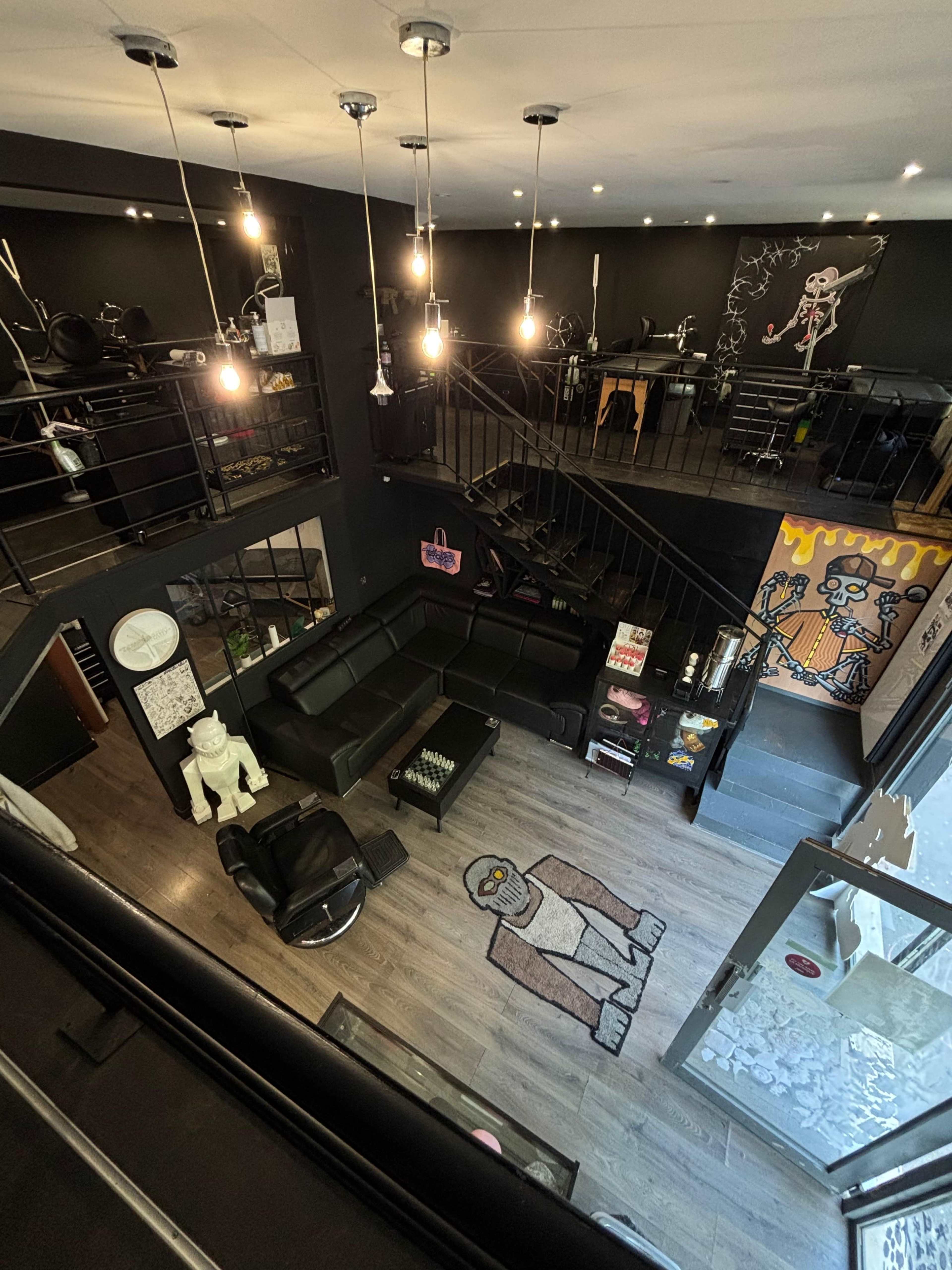 The image shows a stylish, modern interior of a barbershop or salon with dark walls, various art pieces, and multiple seating areas.
