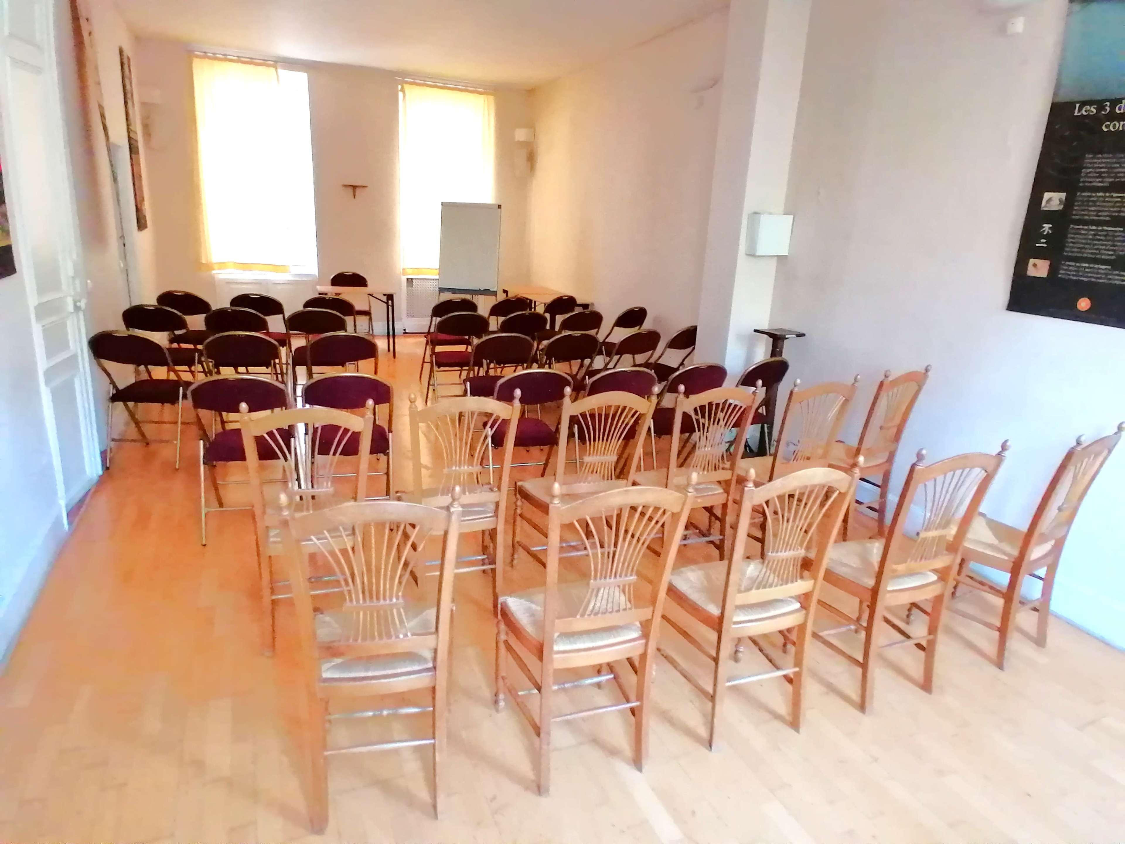 The image shows a room set up for a meeting, featuring rows of empty wooden chairs arranged neatly on a wooden floor.