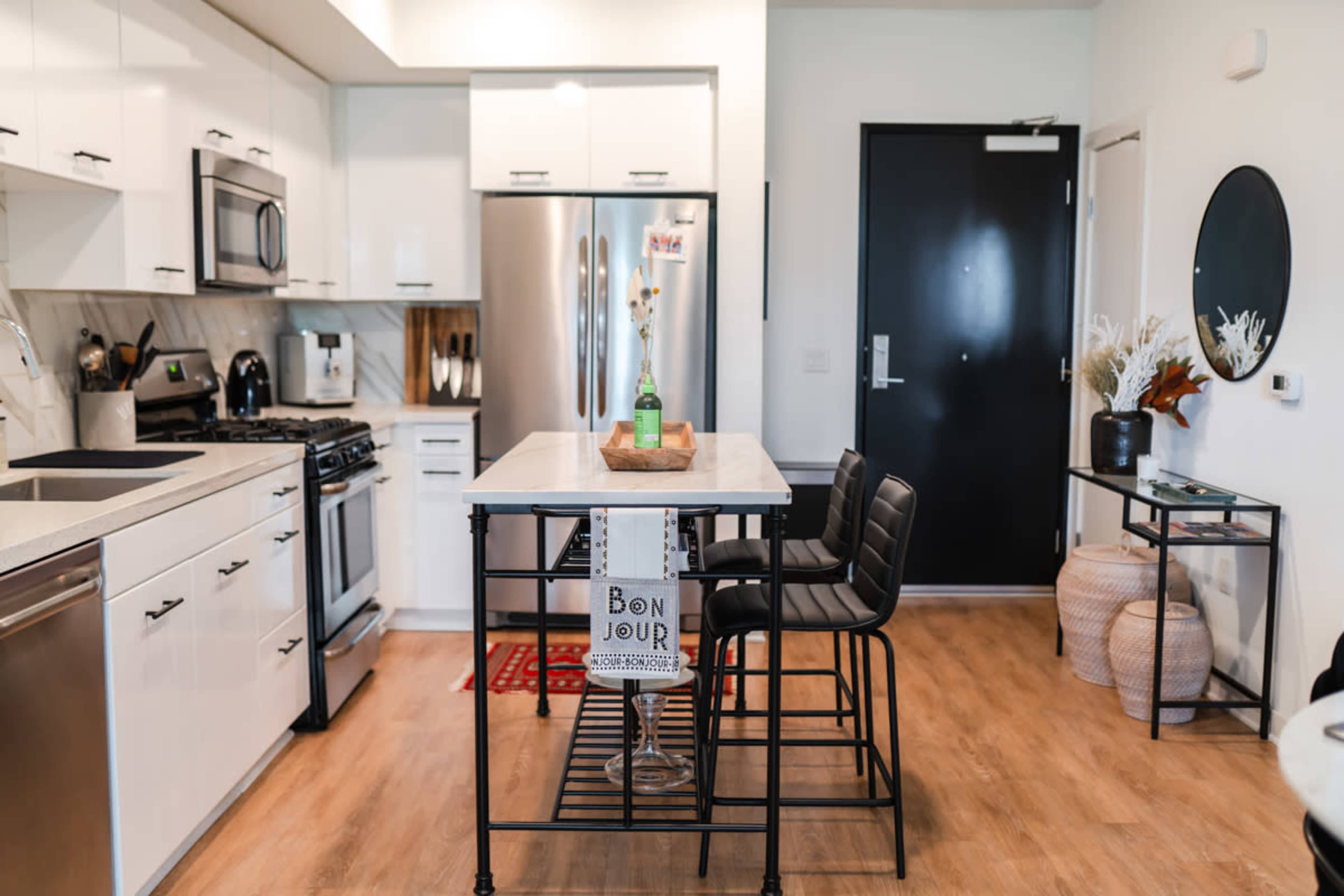 A modern kitchen features sleek white cabinets, stainless steel appliances, and a central island with bar stools.