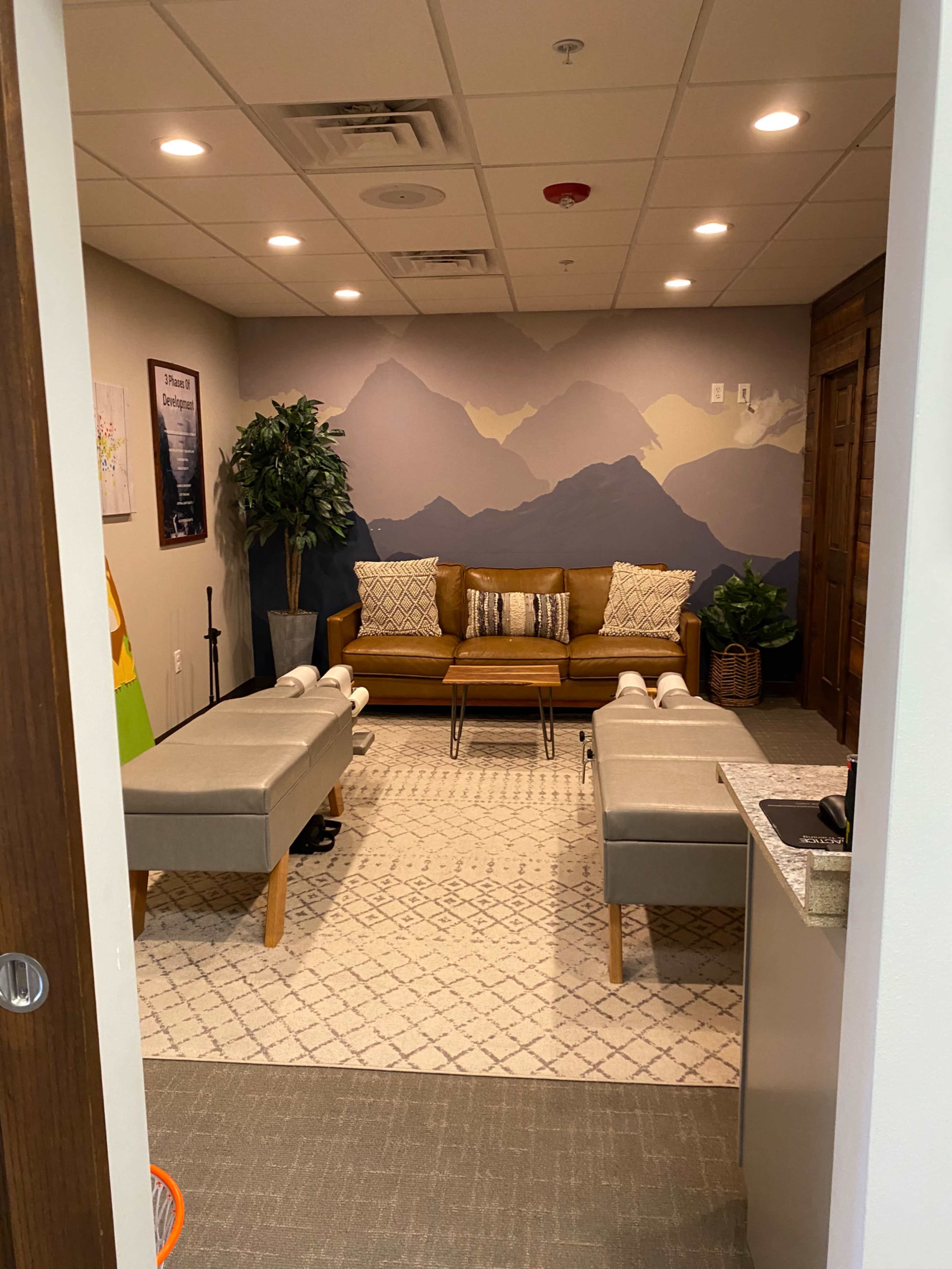 A cozy waiting room featuring a sofa, two benches, and a mountain mural on the wall.