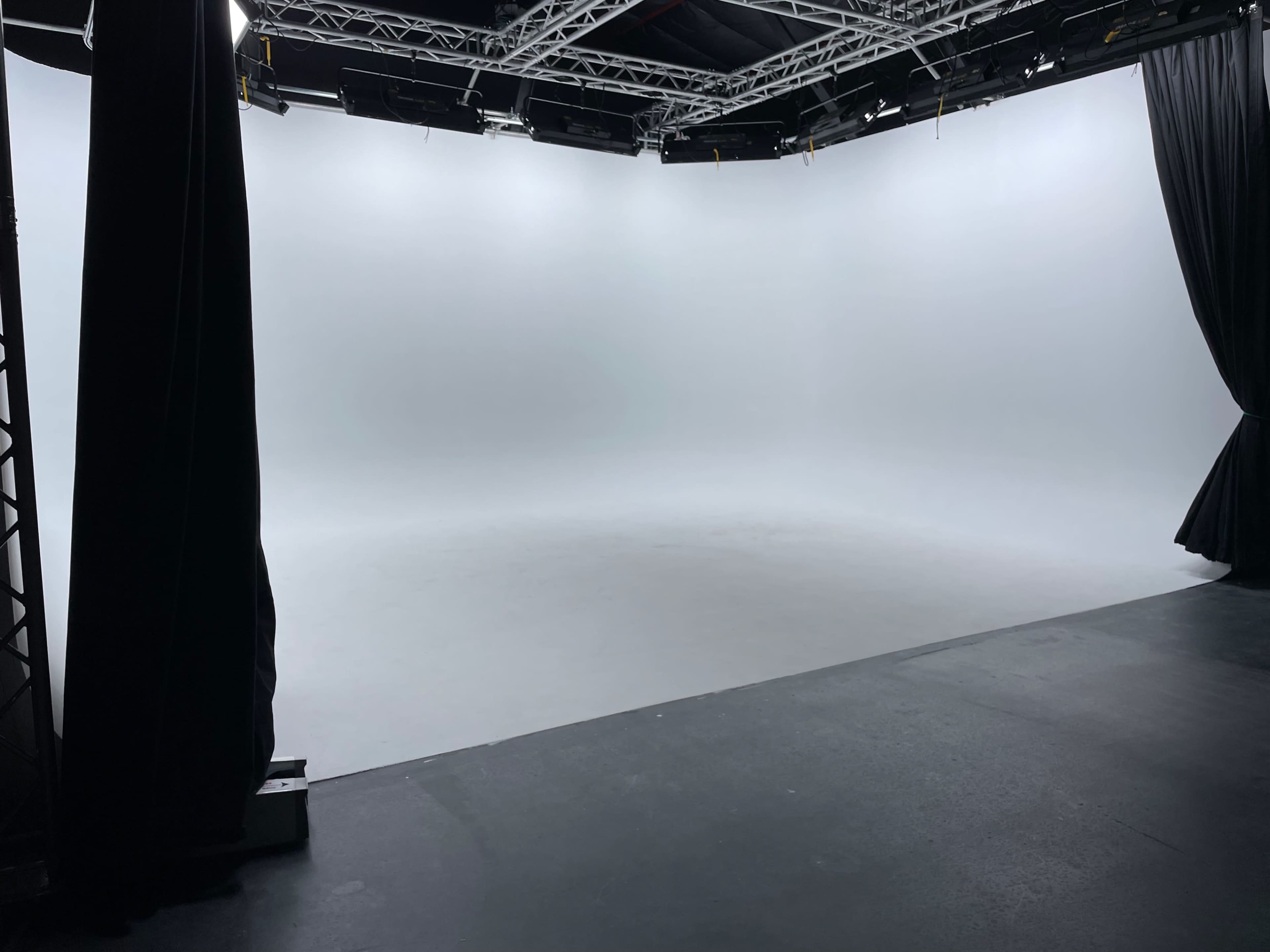 An empty studio space with a seamless white backdrop and overhead lighting.