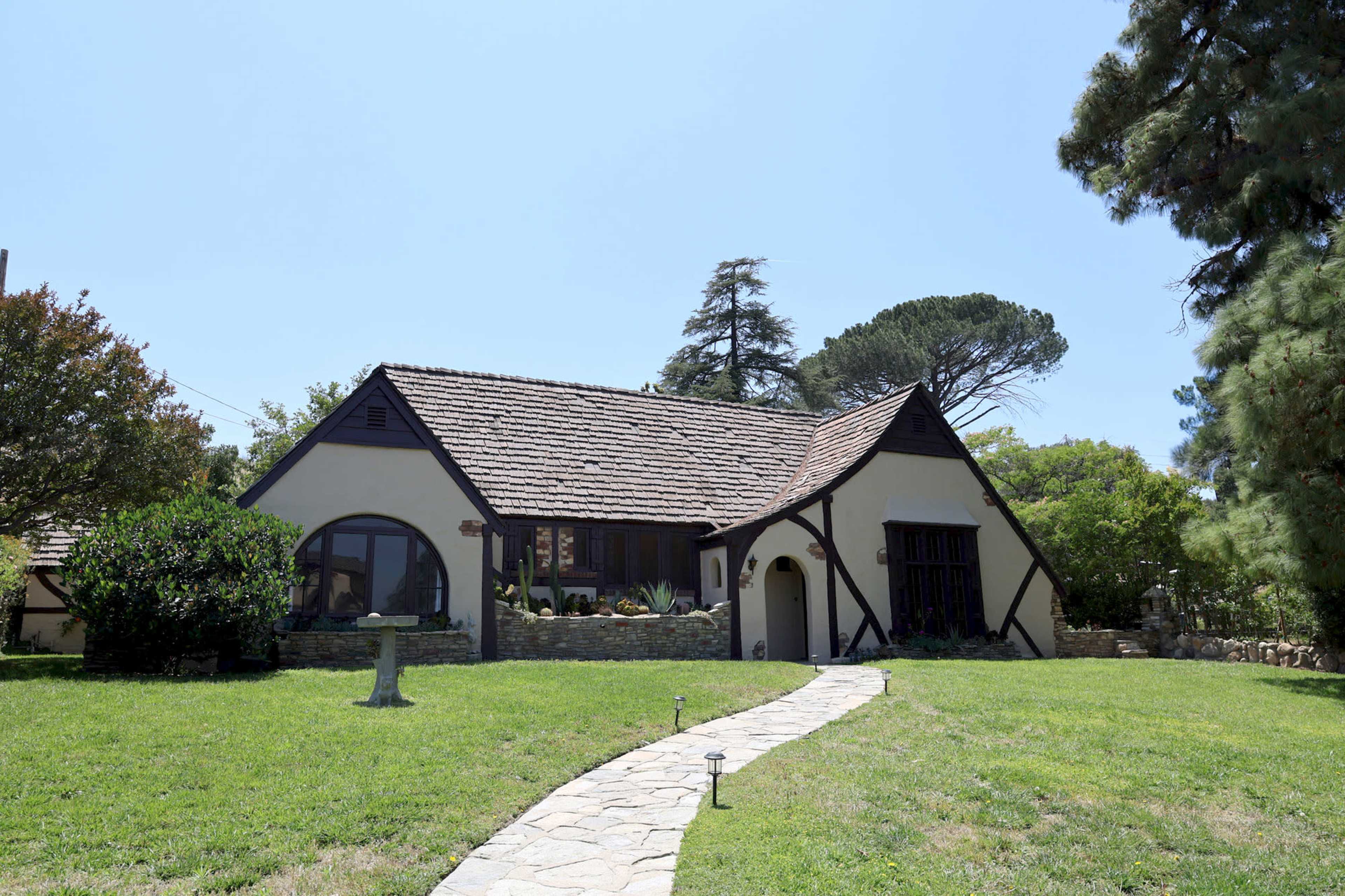 A cottage-style house with a stone pathway and a landscaped yard is situated under a clear blue sky.