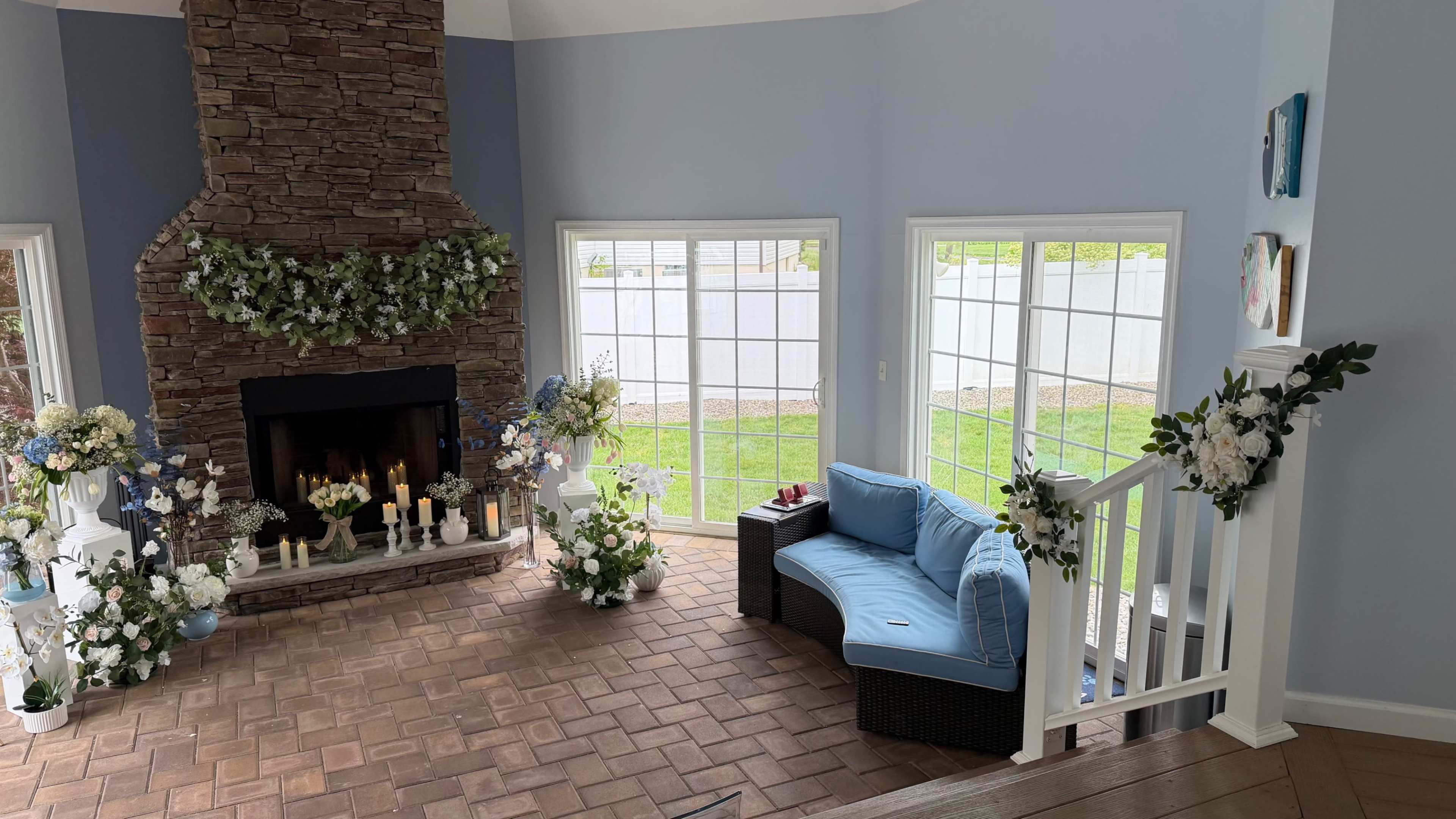 The image shows a living room with a stone fireplace, white French doors leading to a garden, and a blue couch adorned with decorative pillows.