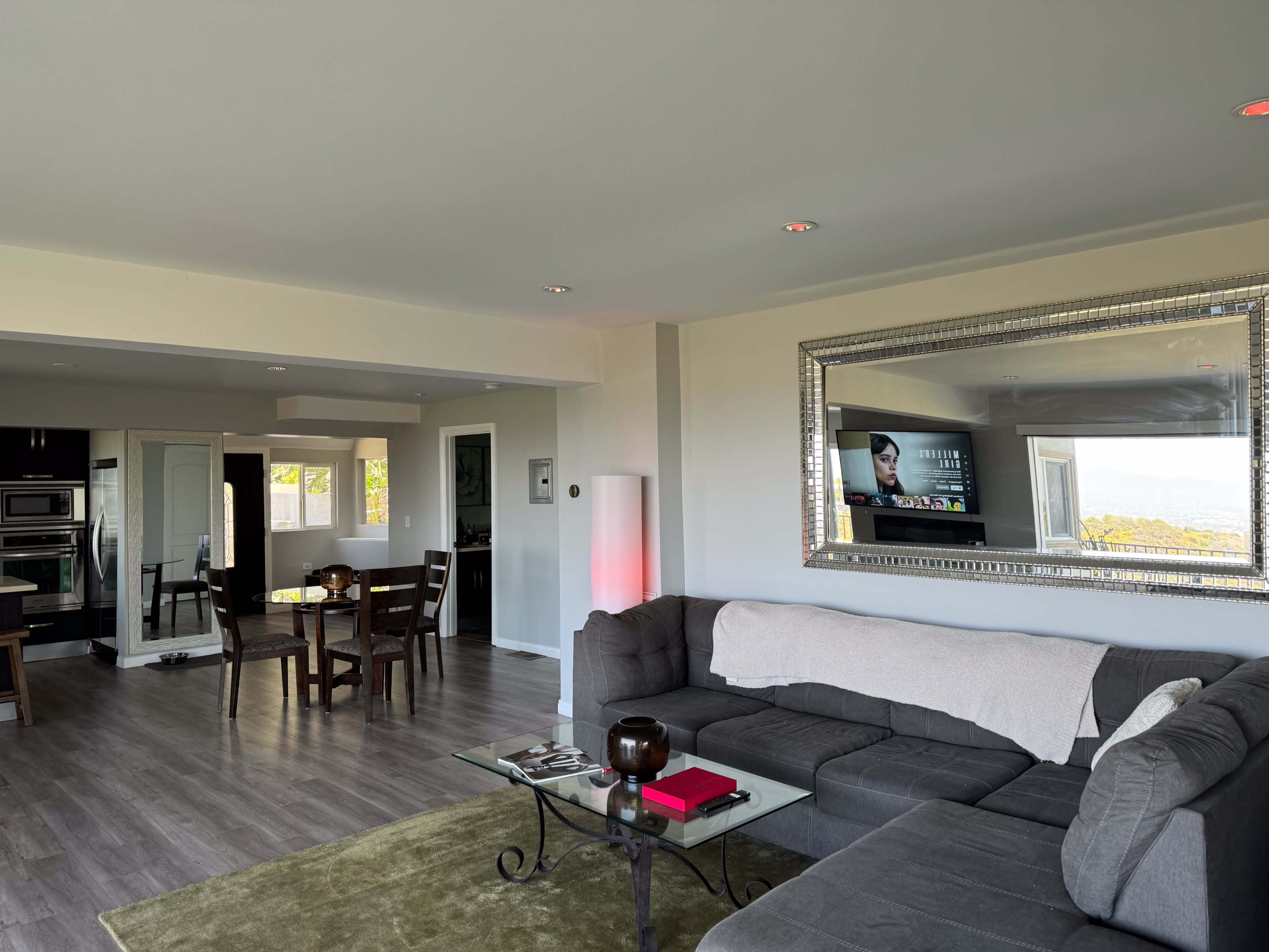 A modern living room with a large sectional sofa, a glass coffee table, and a dining area adjacent to a kitchen.