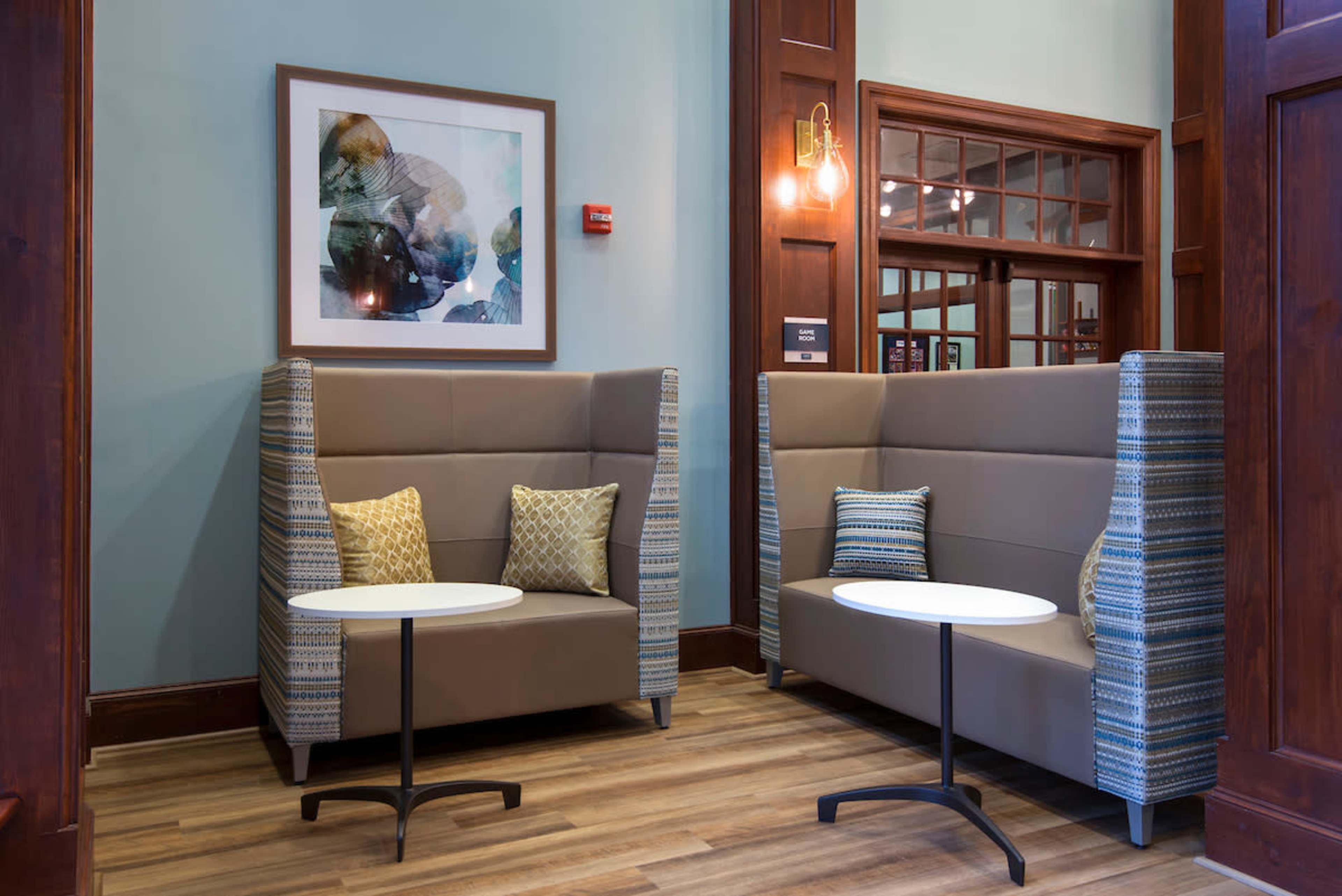 A cozy seating area with two upholstered booths, each paired with a small round table, set against a backdrop of wood paneling and an abstract artwork on the wall.