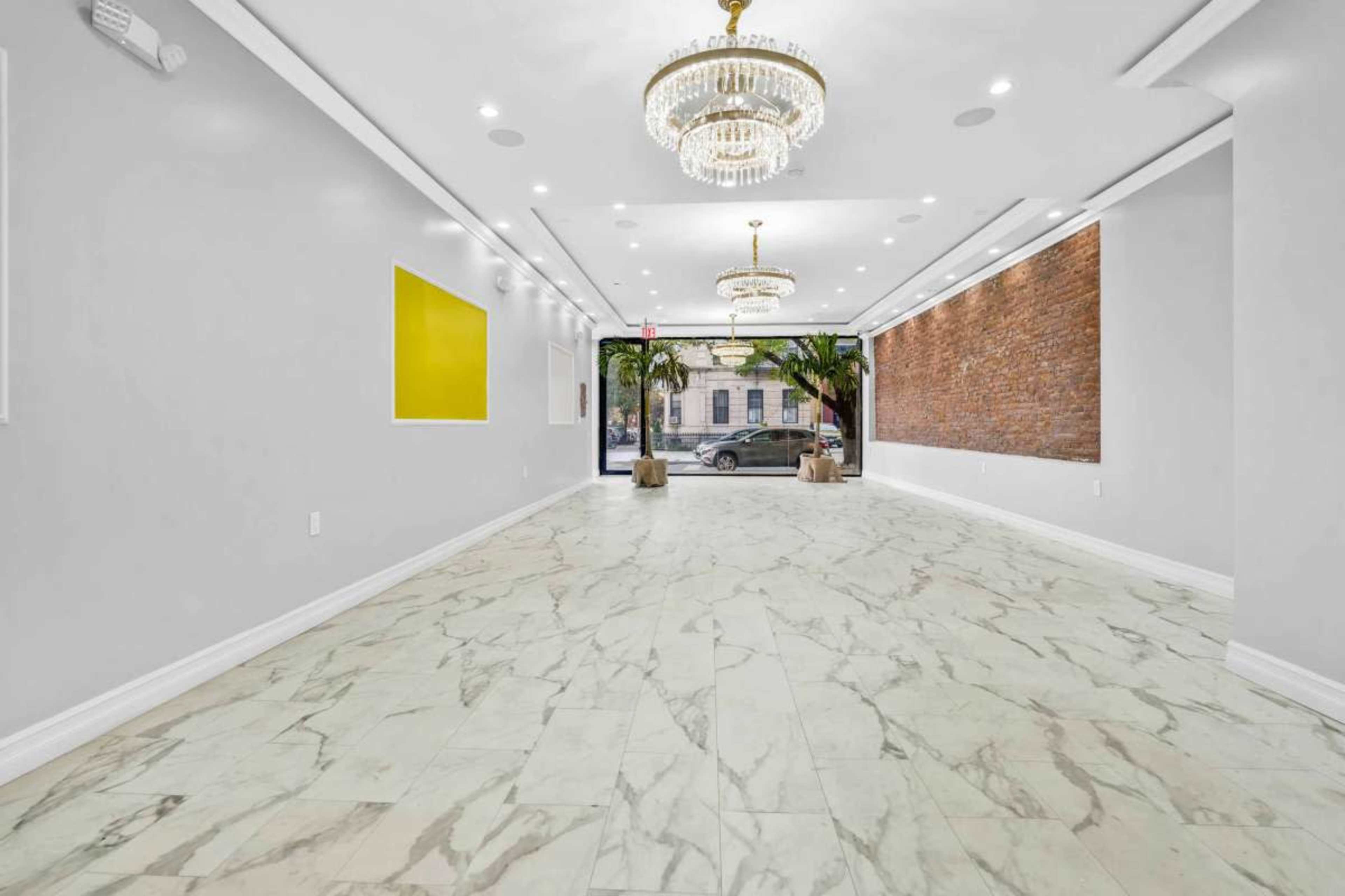 The image shows an empty interior space with marble flooring, two chandeliers, and a large window revealing an exterior view.