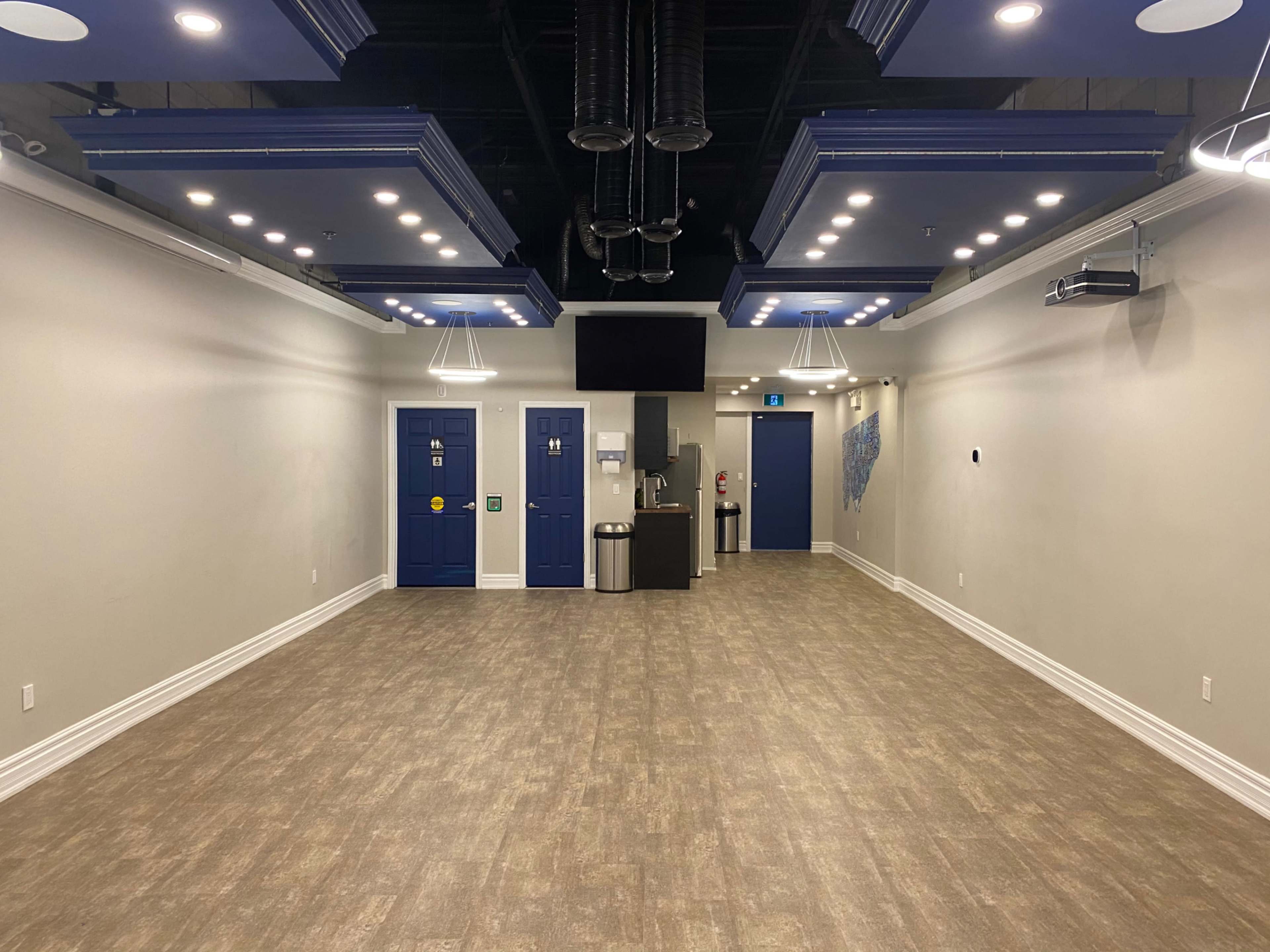 A spacious, well-lit interior room with blue doors and a kitchenette area on one side.