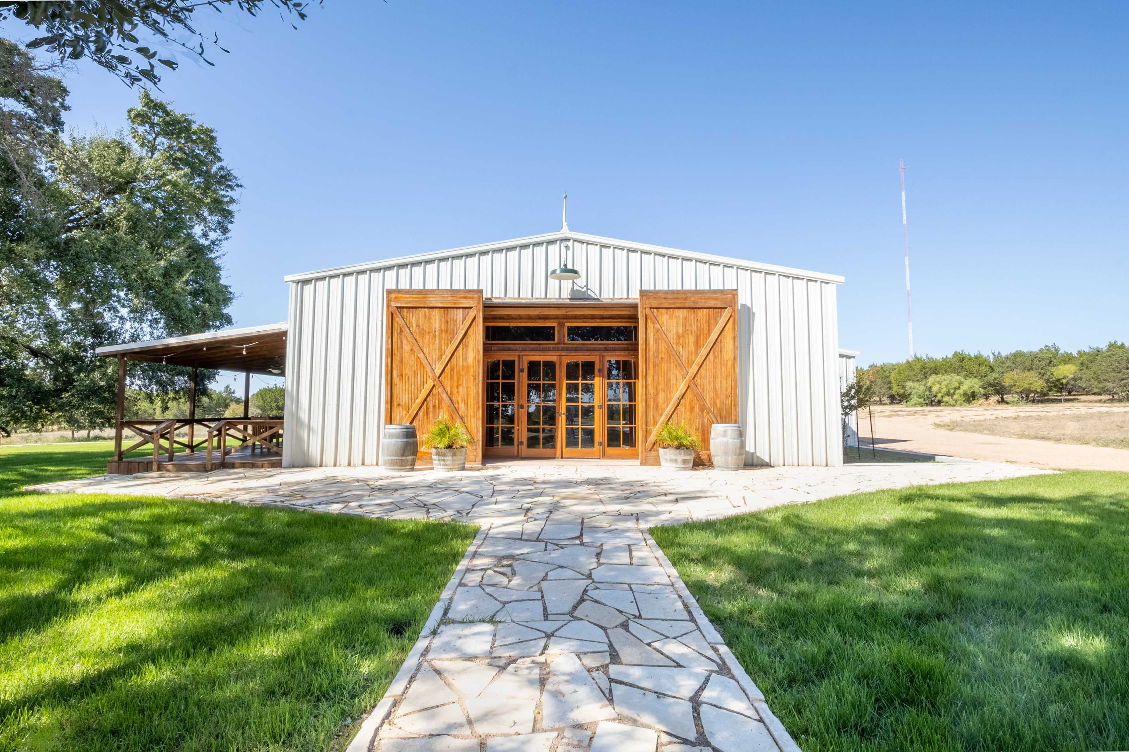 A large metal barn with wooden double doors and a stone pathway leads to its entrance, surrounded by green grass and trees.