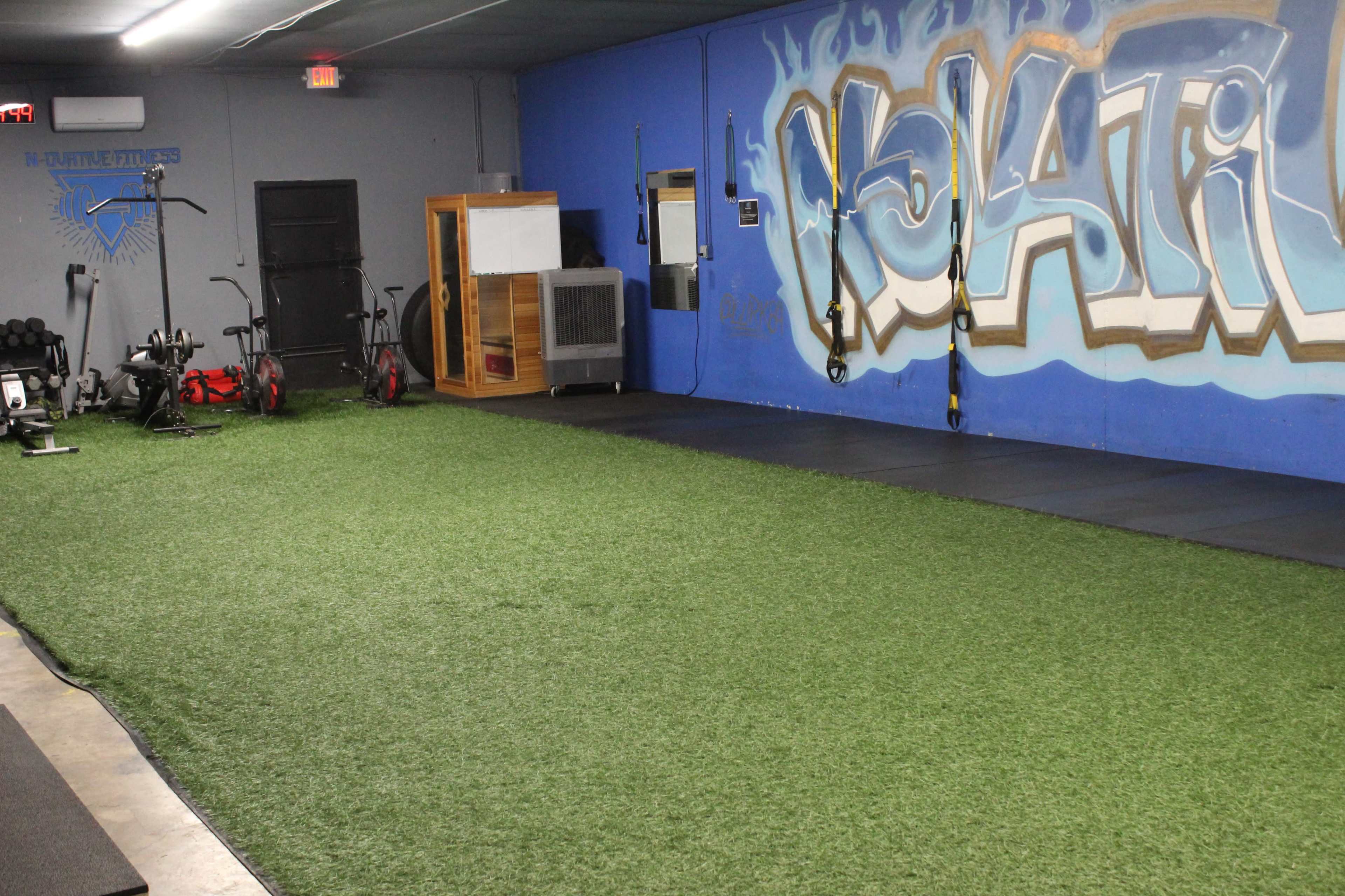 A fitness space with artificial turf, exercise equipment, and a large graffiti mural on the wall.