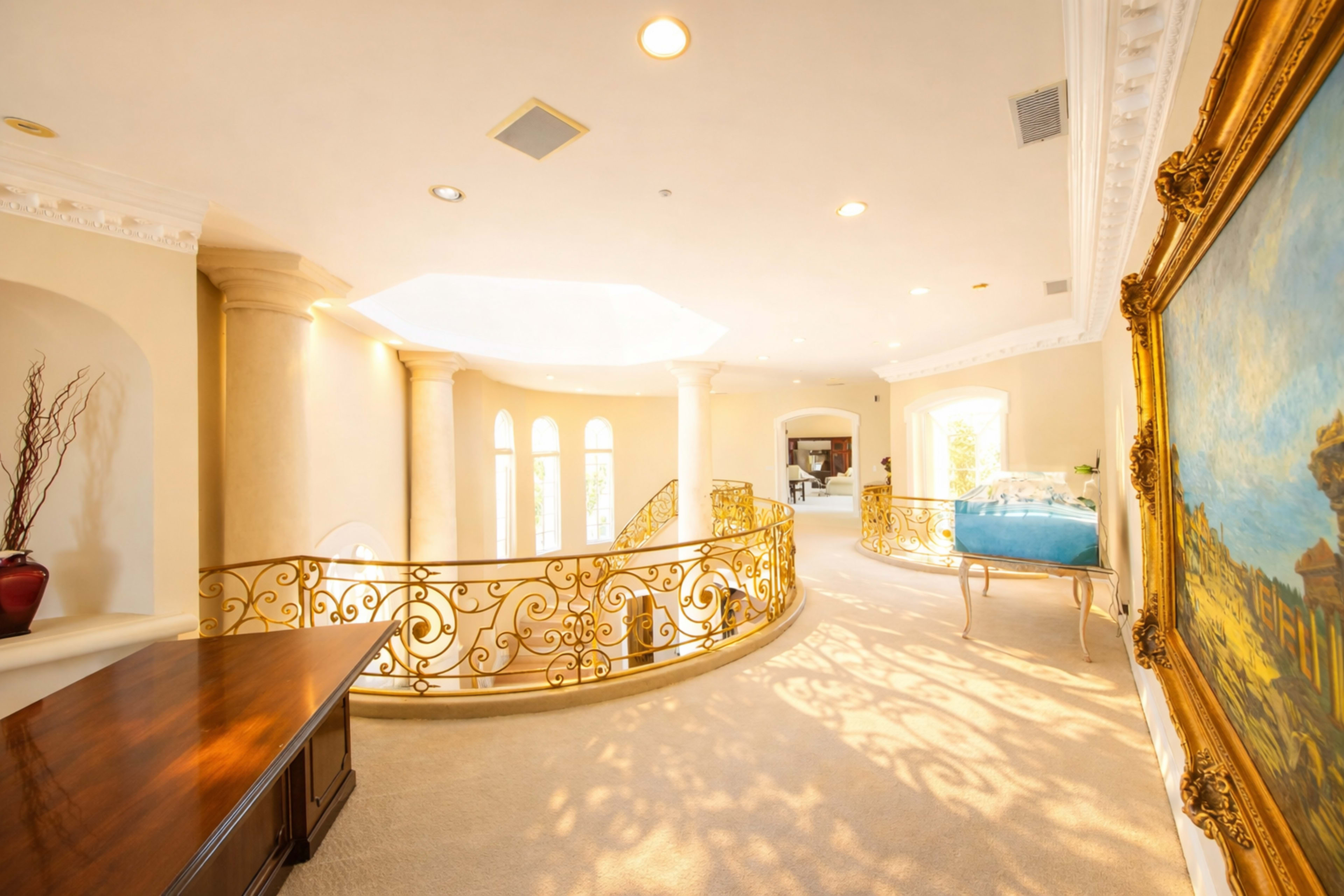 The scene features a spacious, elegantly designed hallway with a decorative railing, abundant natural light, and an ornate painting on the wall.