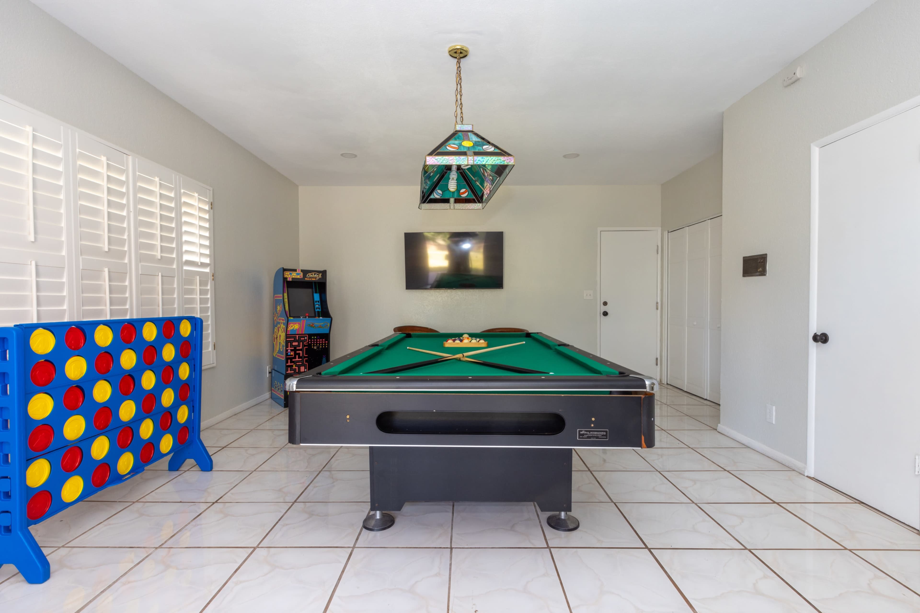 A game room featuring a pool table, a Connect Four game, an arcade machine, and a television mounted on the wall.
