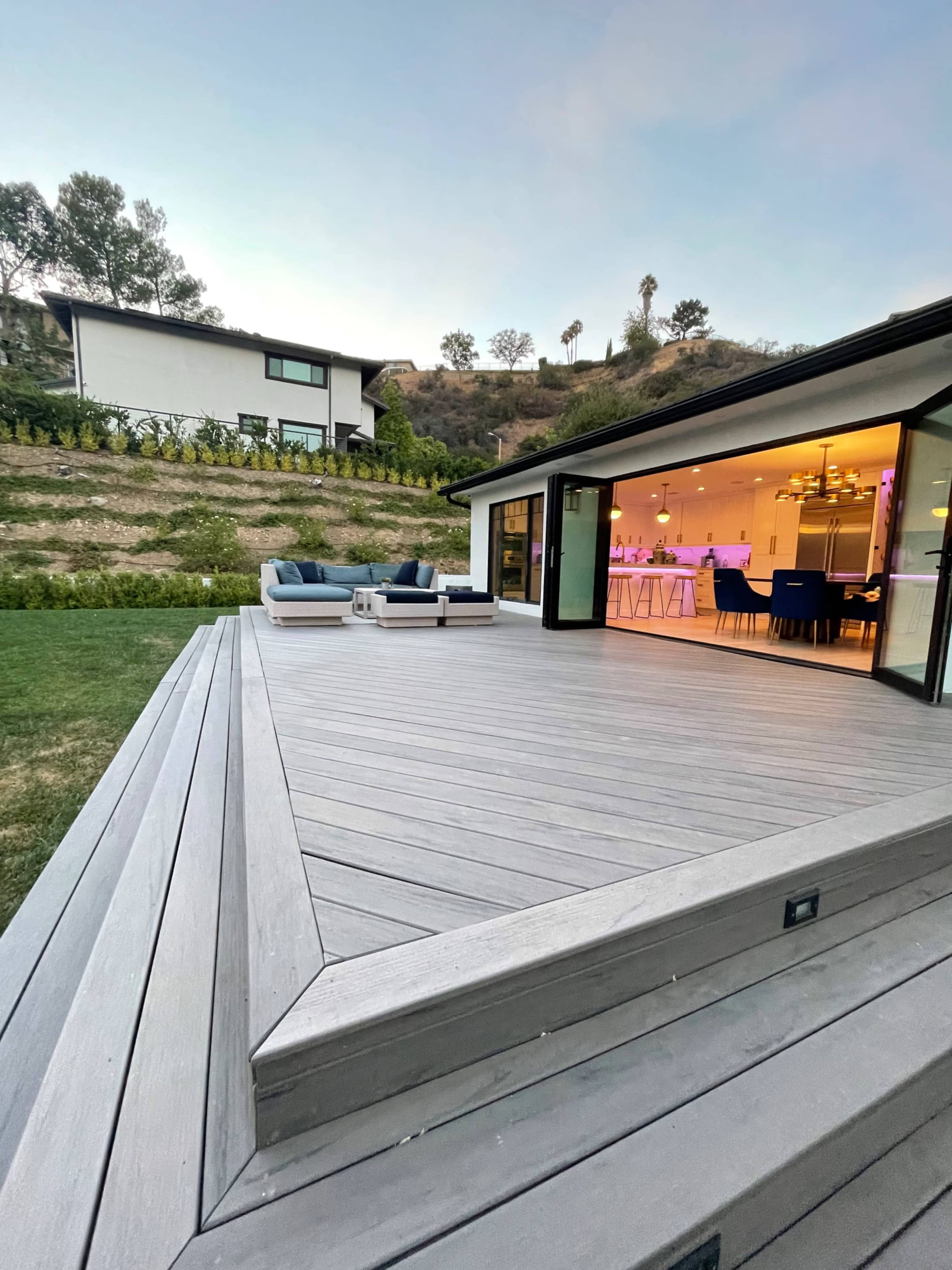 A modern deck leading to an open-concept living space with a view of a hillside and adjacent buildings.