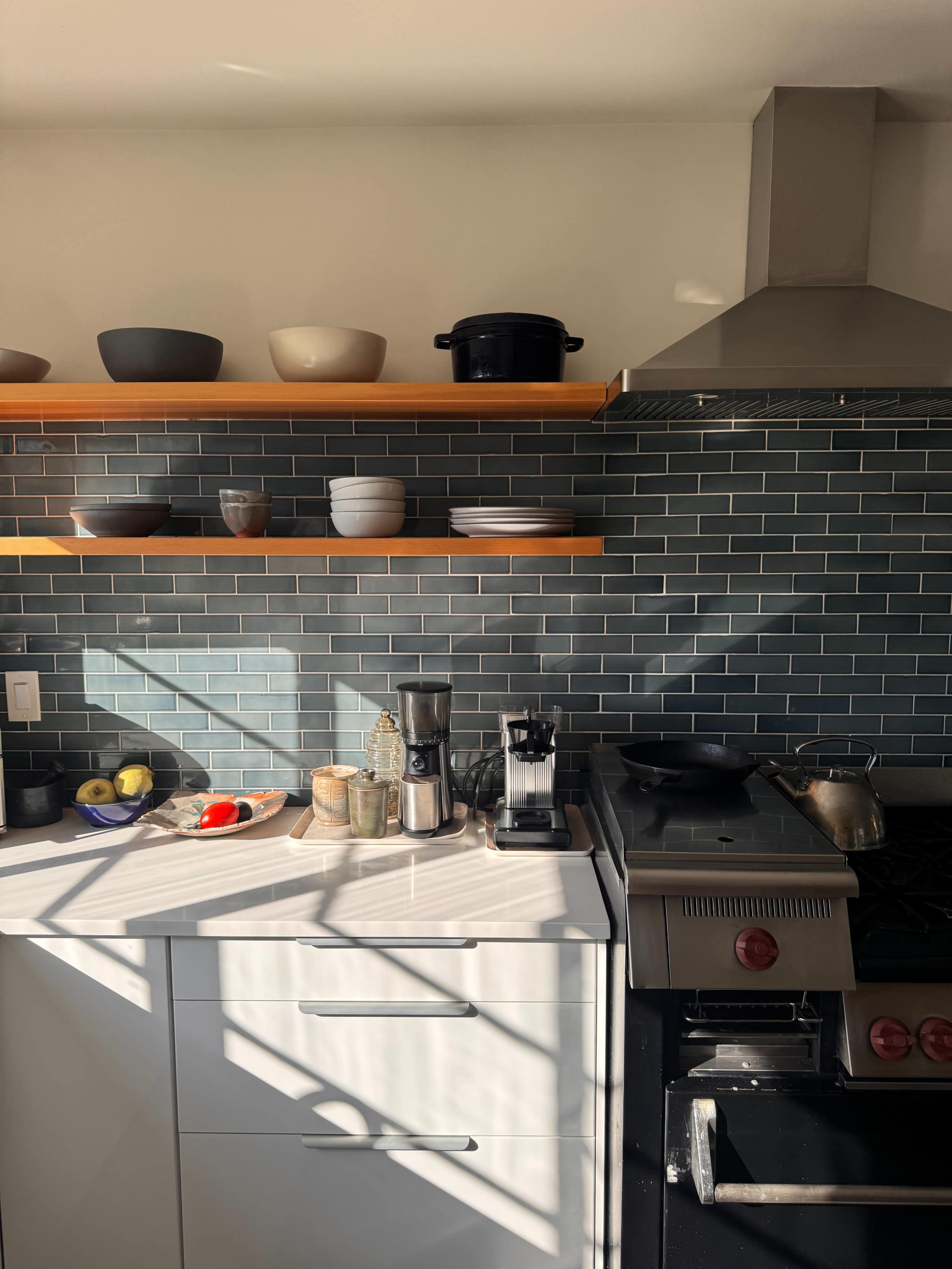 A modern kitchen features a stone counter, gas stove, coffee maker, and shelves displaying various bowls.