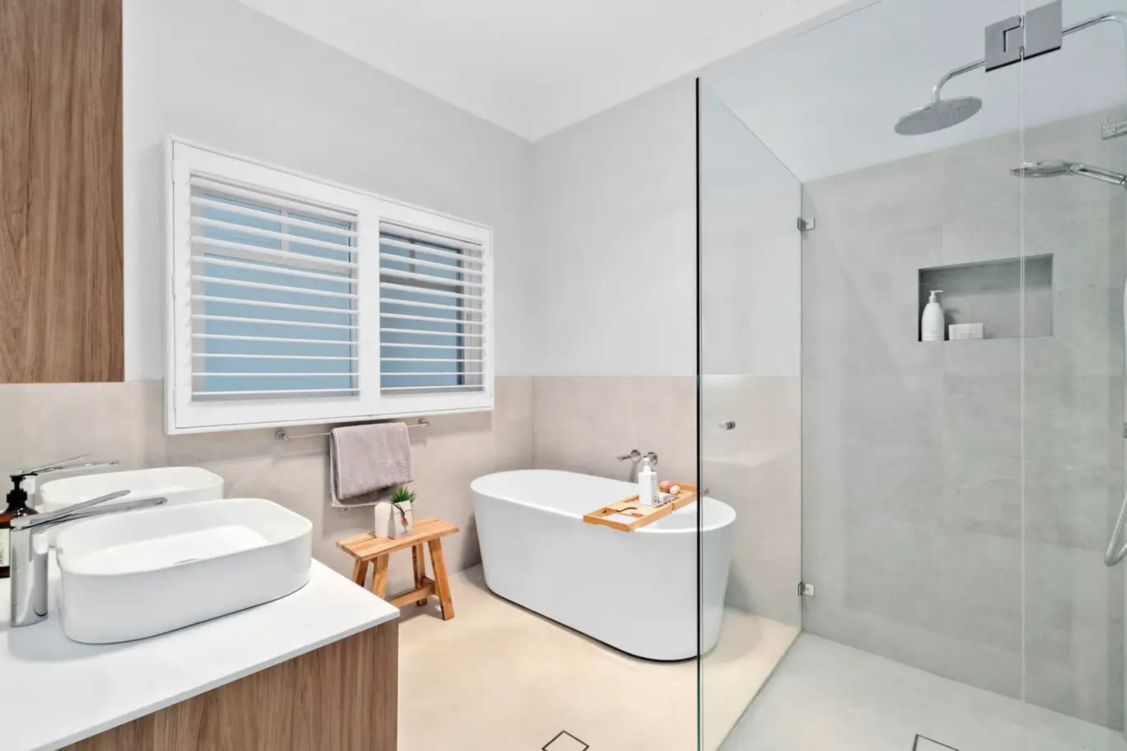 The image shows a modern bathroom featuring a freestanding bathtub, a walk-in shower with a glass enclosure, and dual sinks on a wooden vanity.