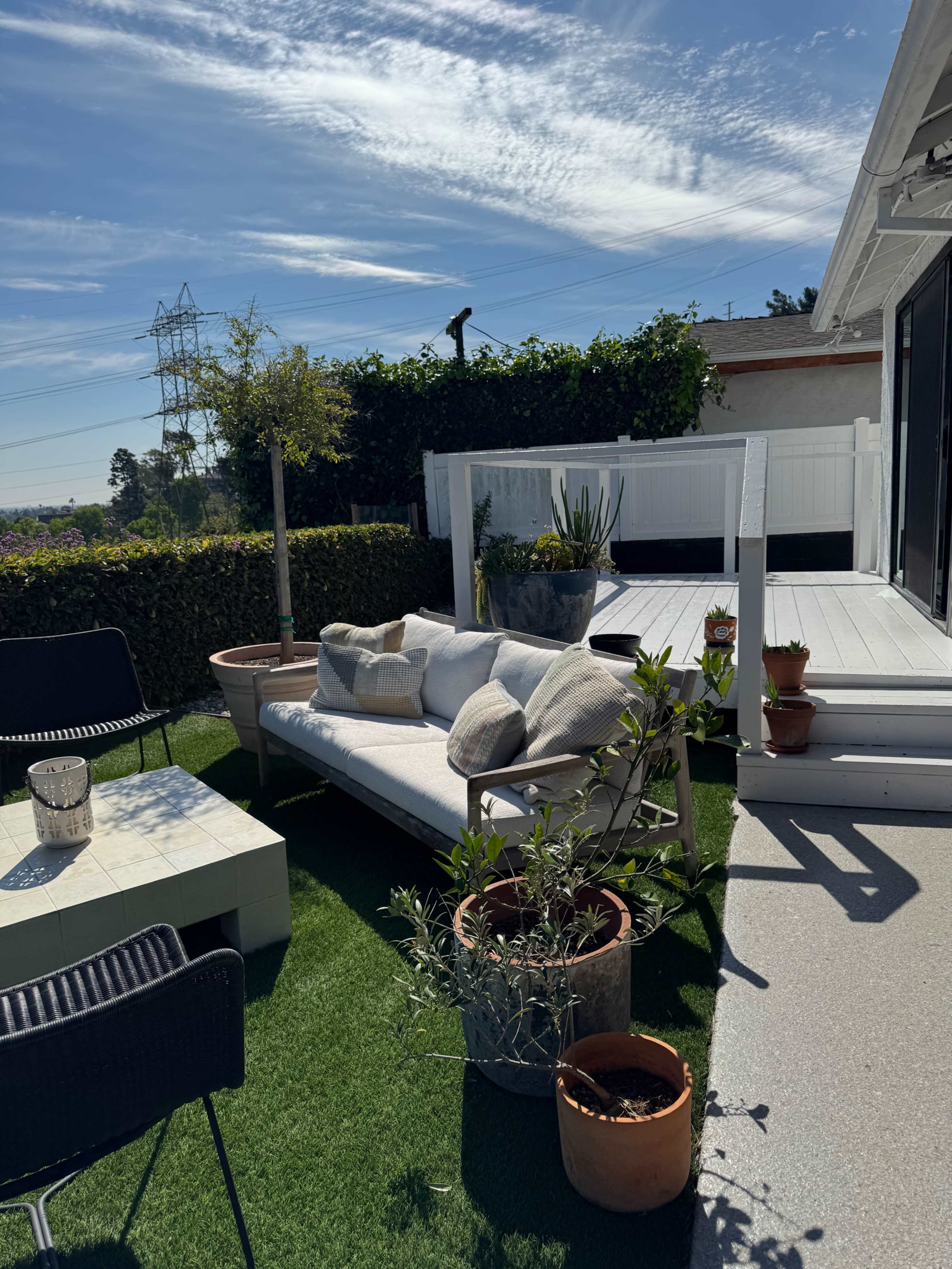 The image shows a landscaped outdoor patio area with a seating arrangement, potted plants, and a wooden deck.