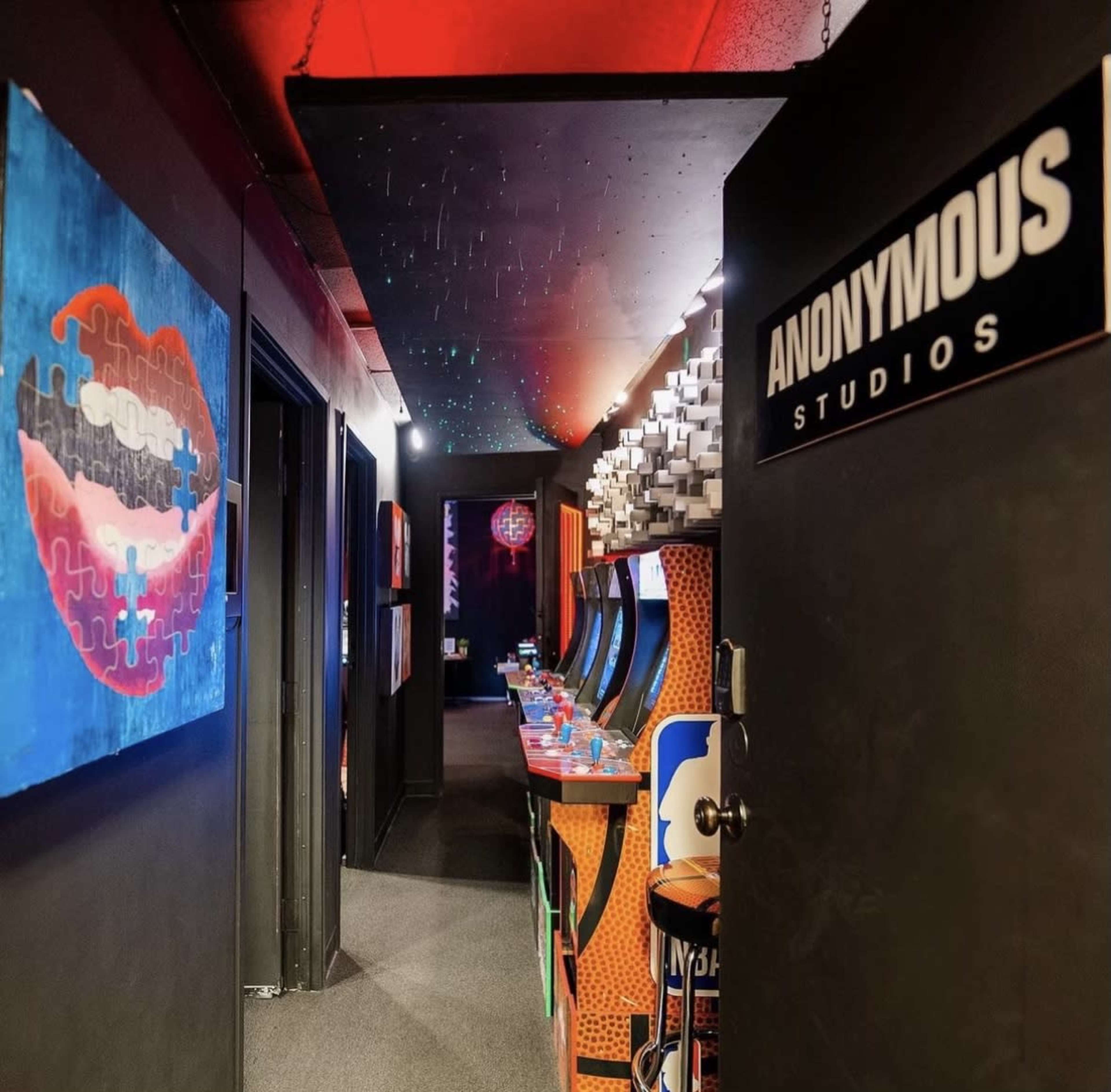 A hallway leading to a studio with arcade game machines on one side and an artistic painting on the wall.