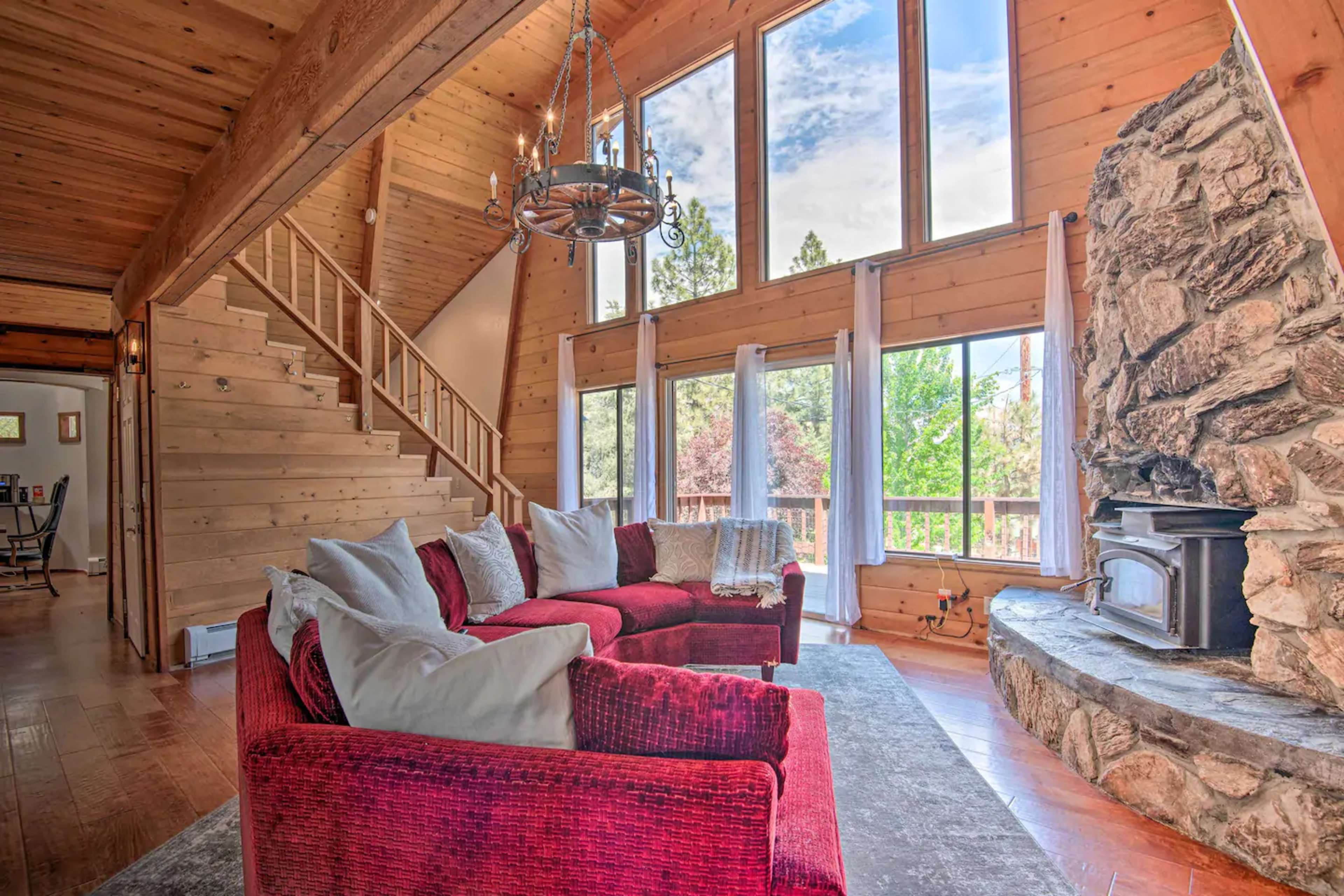 A cozy living room with a red sectional sofa, a stone fireplace, and large windows letting in natural light.