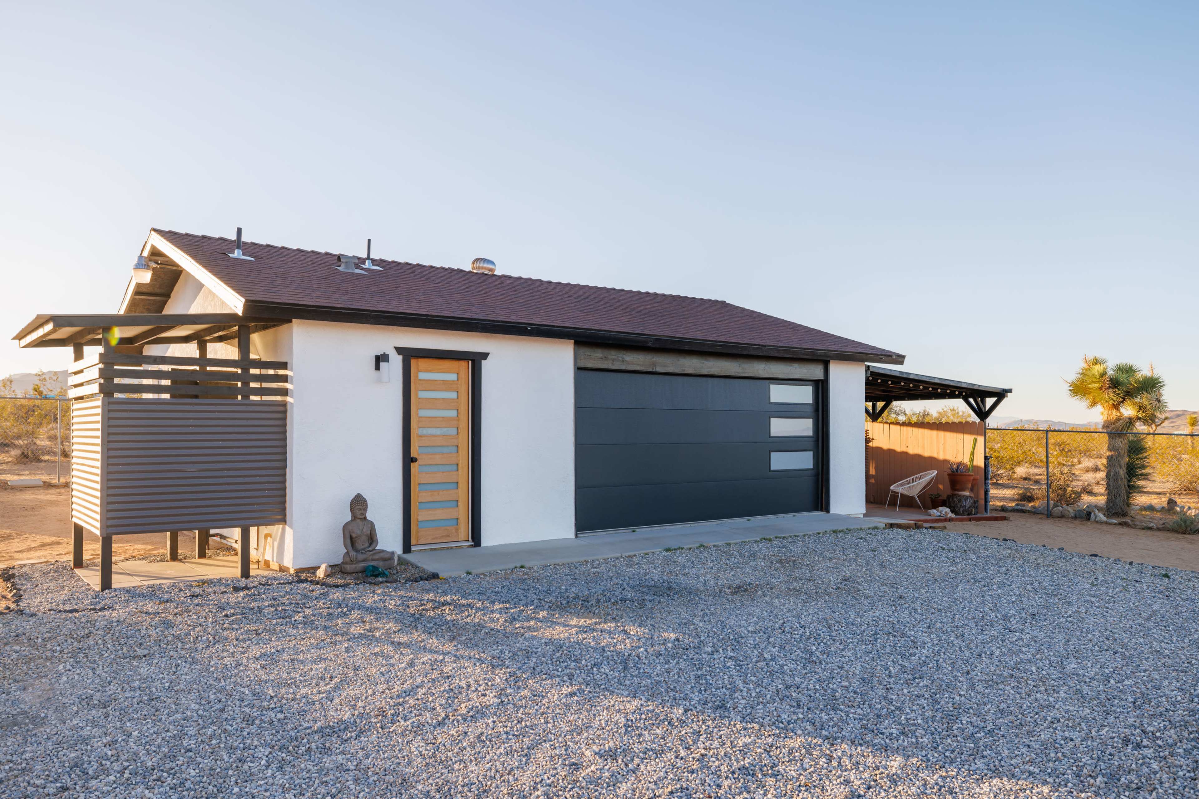 A modern single-story house features a gray and white exterior with a distinctive front door and a gravel driveway.