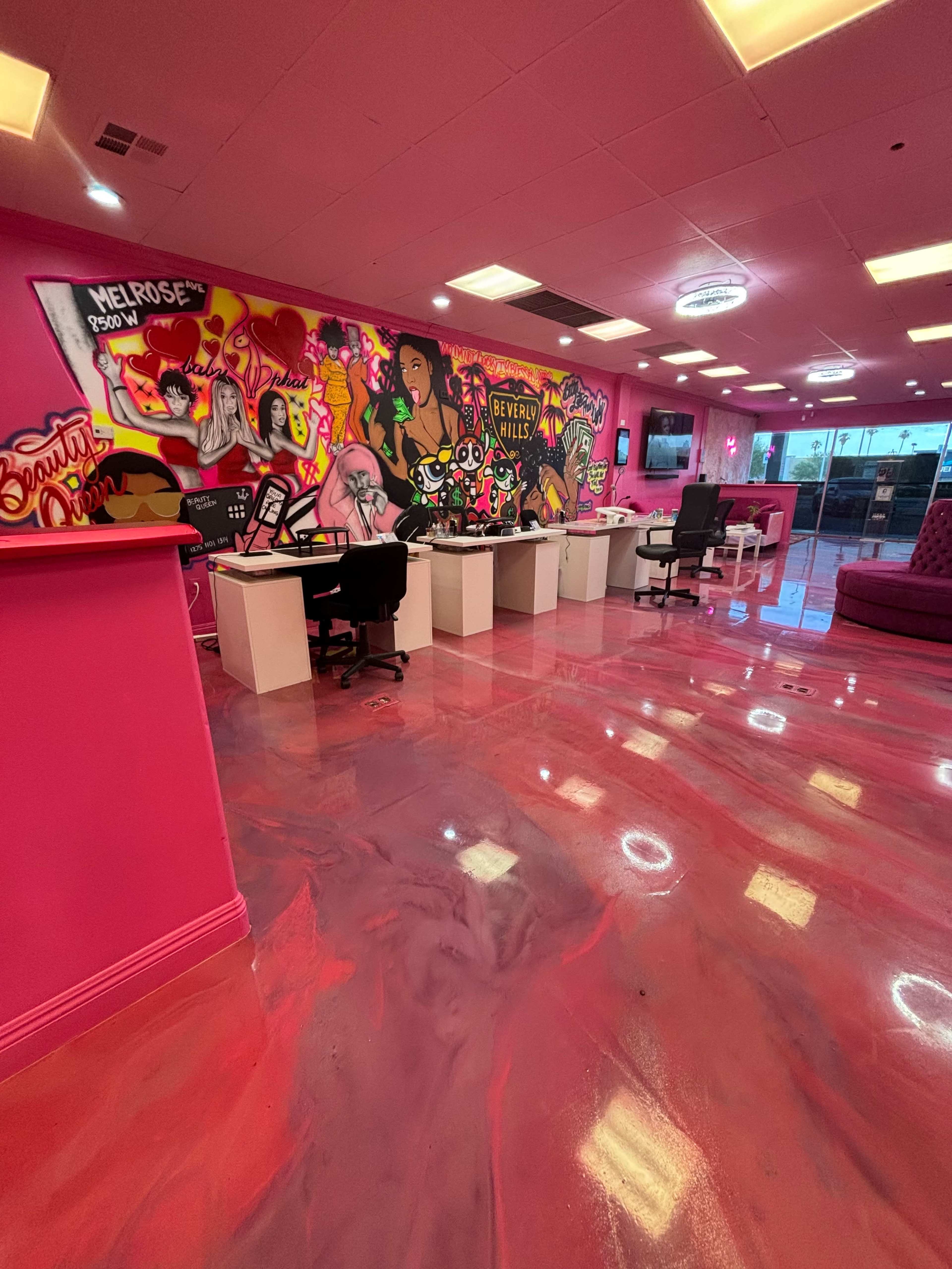 The image shows a vibrant interior space featuring pink walls adorned with colorful graffiti art, multiple workstations with chairs, and a shiny pink floor.