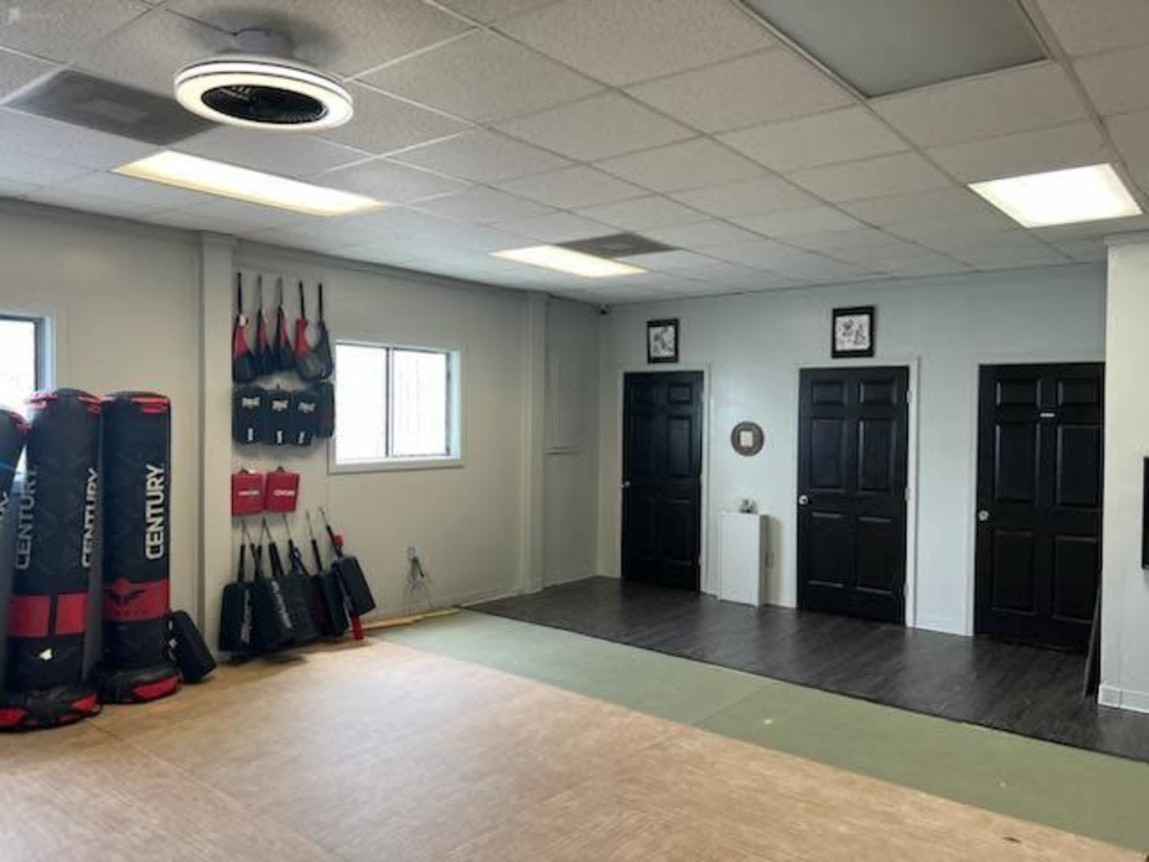 A martial arts training room featuring punching bags on the left wall and two closed black doors on the right.