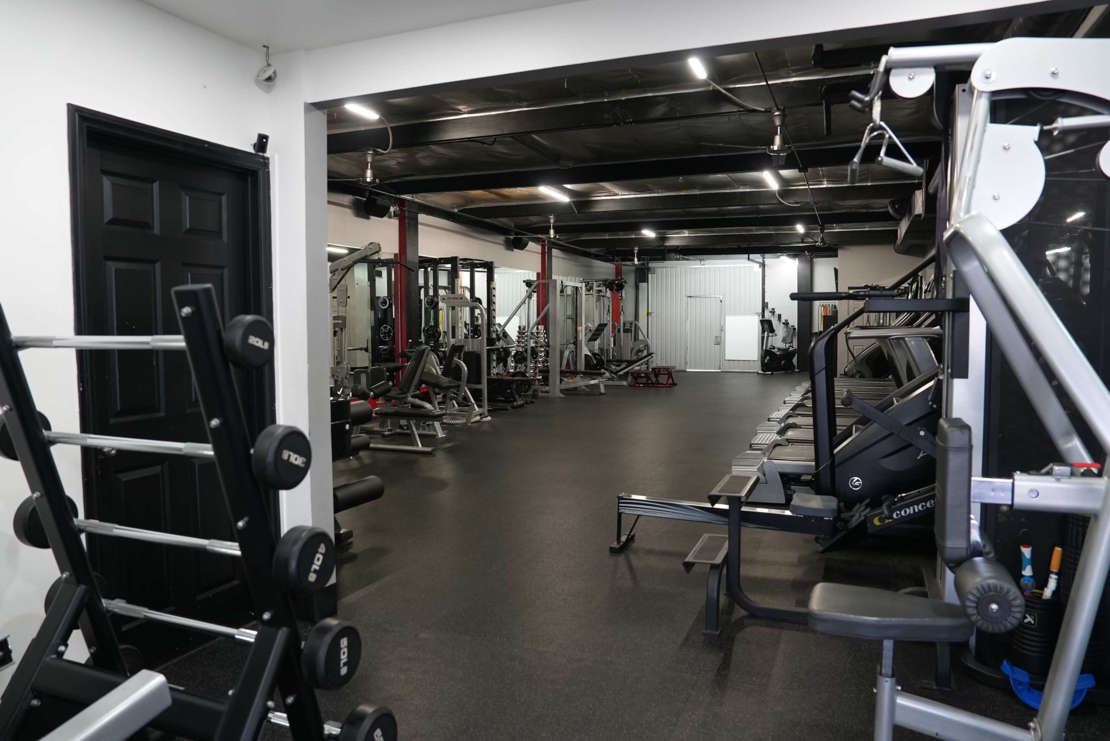 A gym interior featuring various weightlifting equipment and workout stations arranged neatly along the walls.