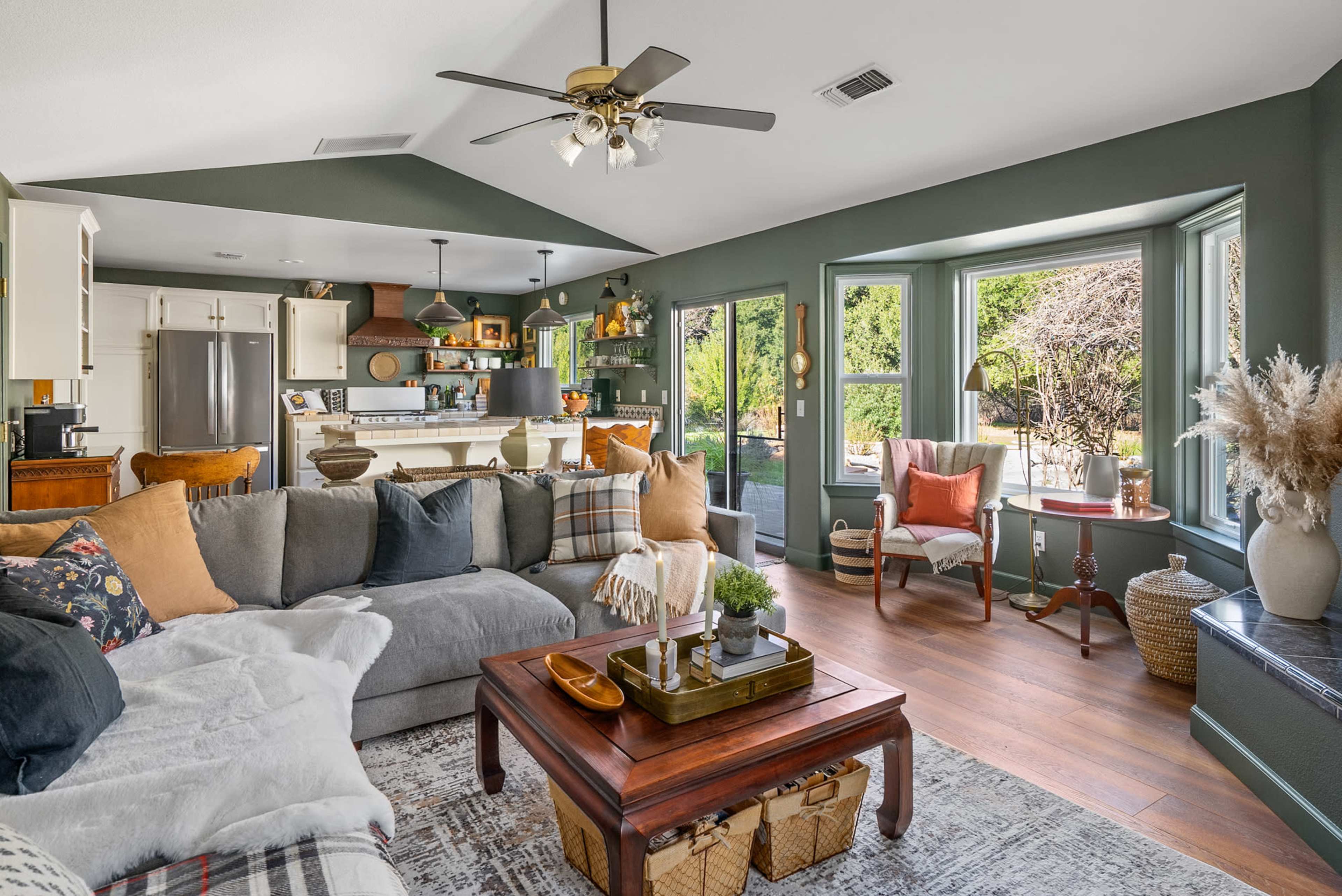 A spacious living room features a large sectional sofa, a wooden coffee table, and large windows with views of greenery.