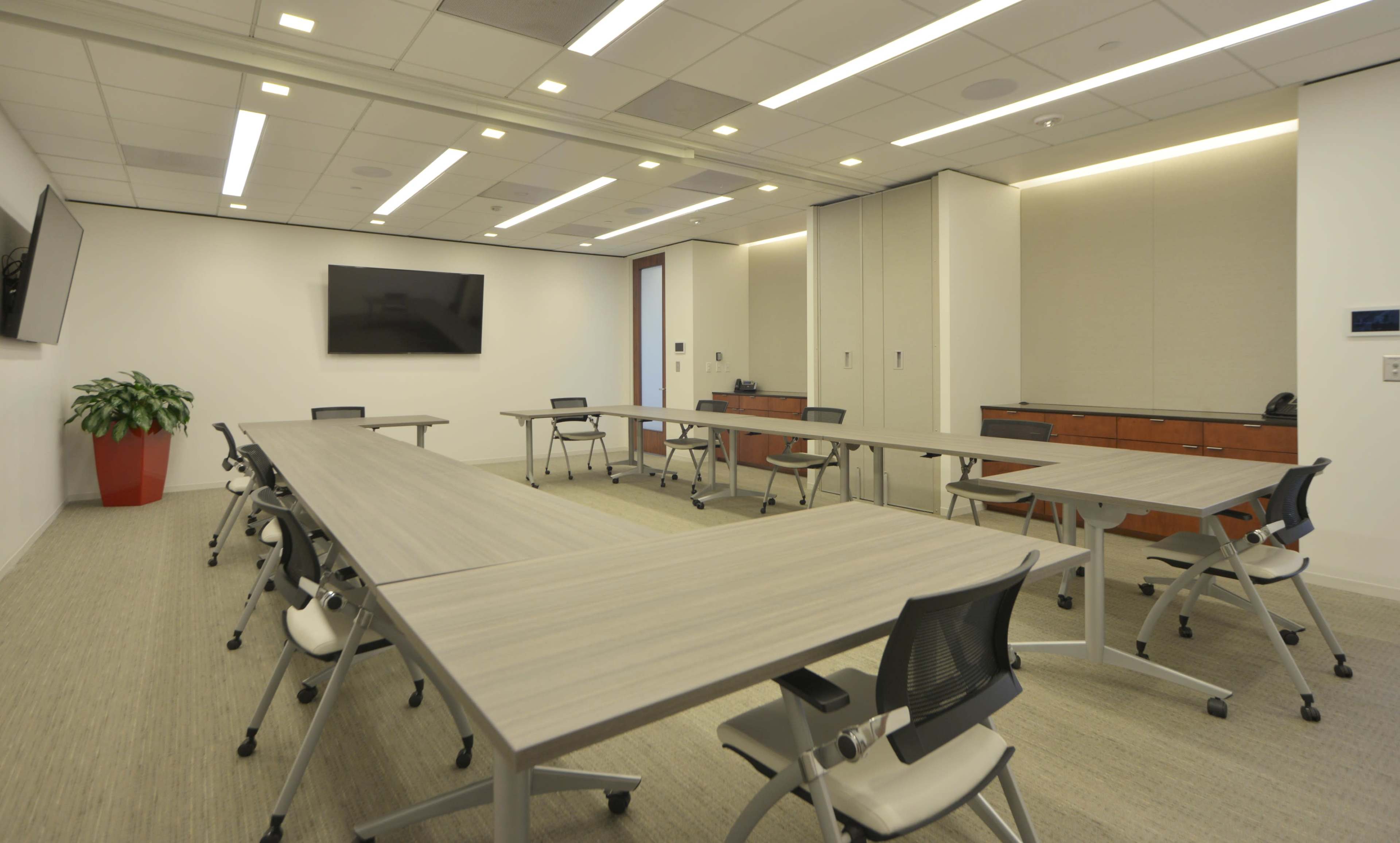 A modern conference room features multiple tables arranged for meetings, with chairs and a wall-mounted screen.