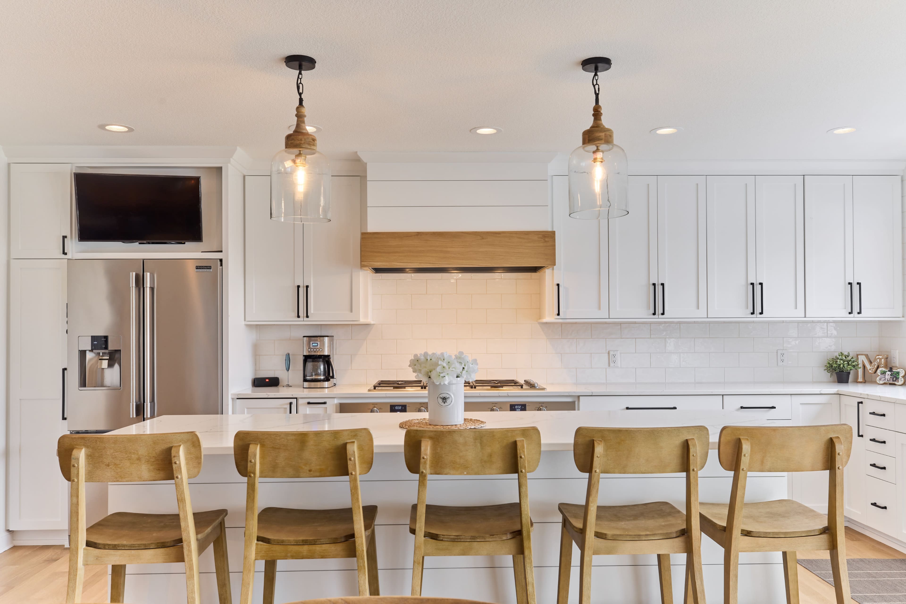 A modern kitchen features white cabinetry, a large island with wooden stools, and pendant lighting above.