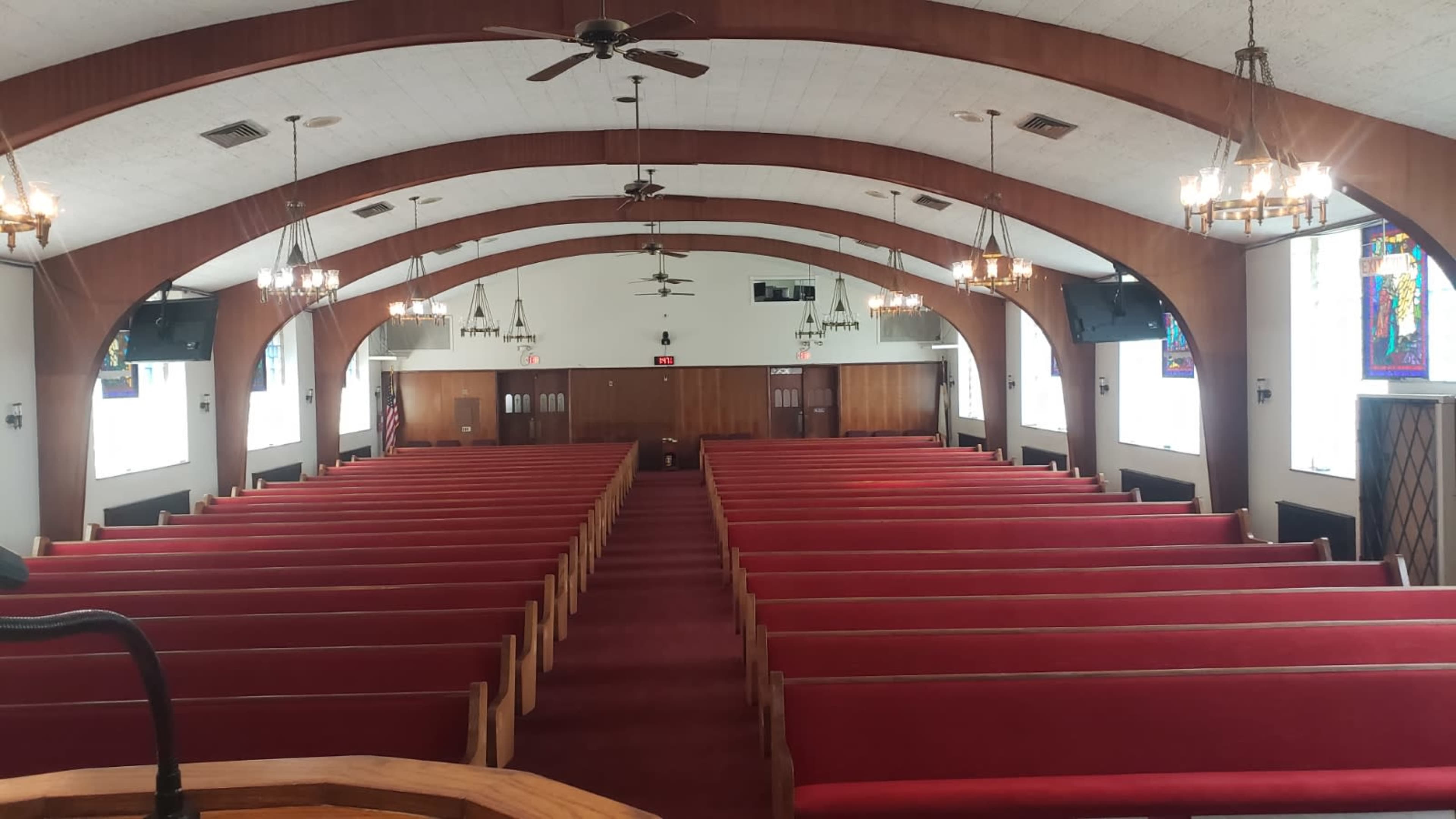 The image shows the interior of a church with rows of red pews arranged symmetrically around a central aisle.