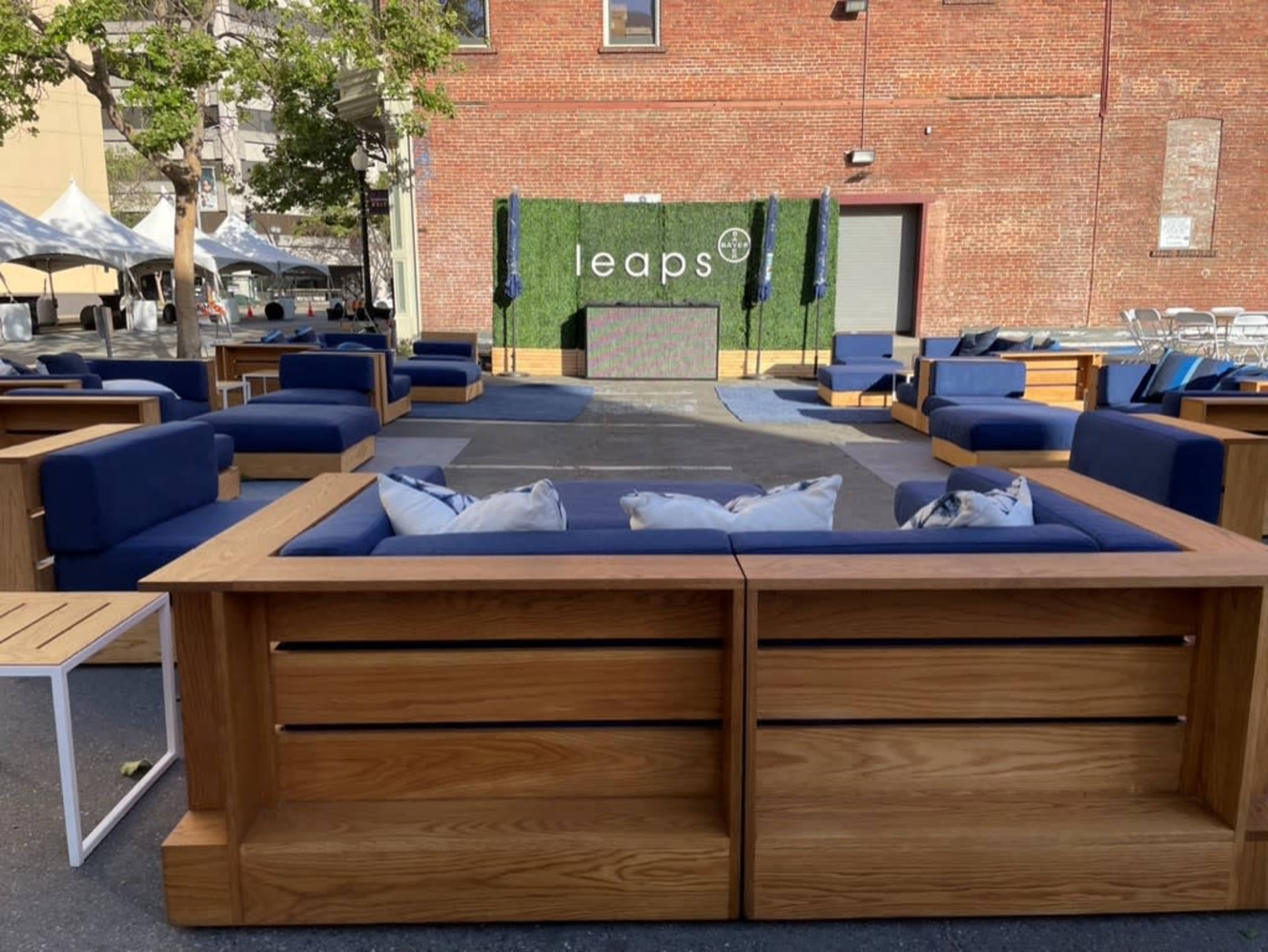 A modern outdoor lounge area with wooden seating arranged around a central stage marked with the word "leaps" on a green backdrop.