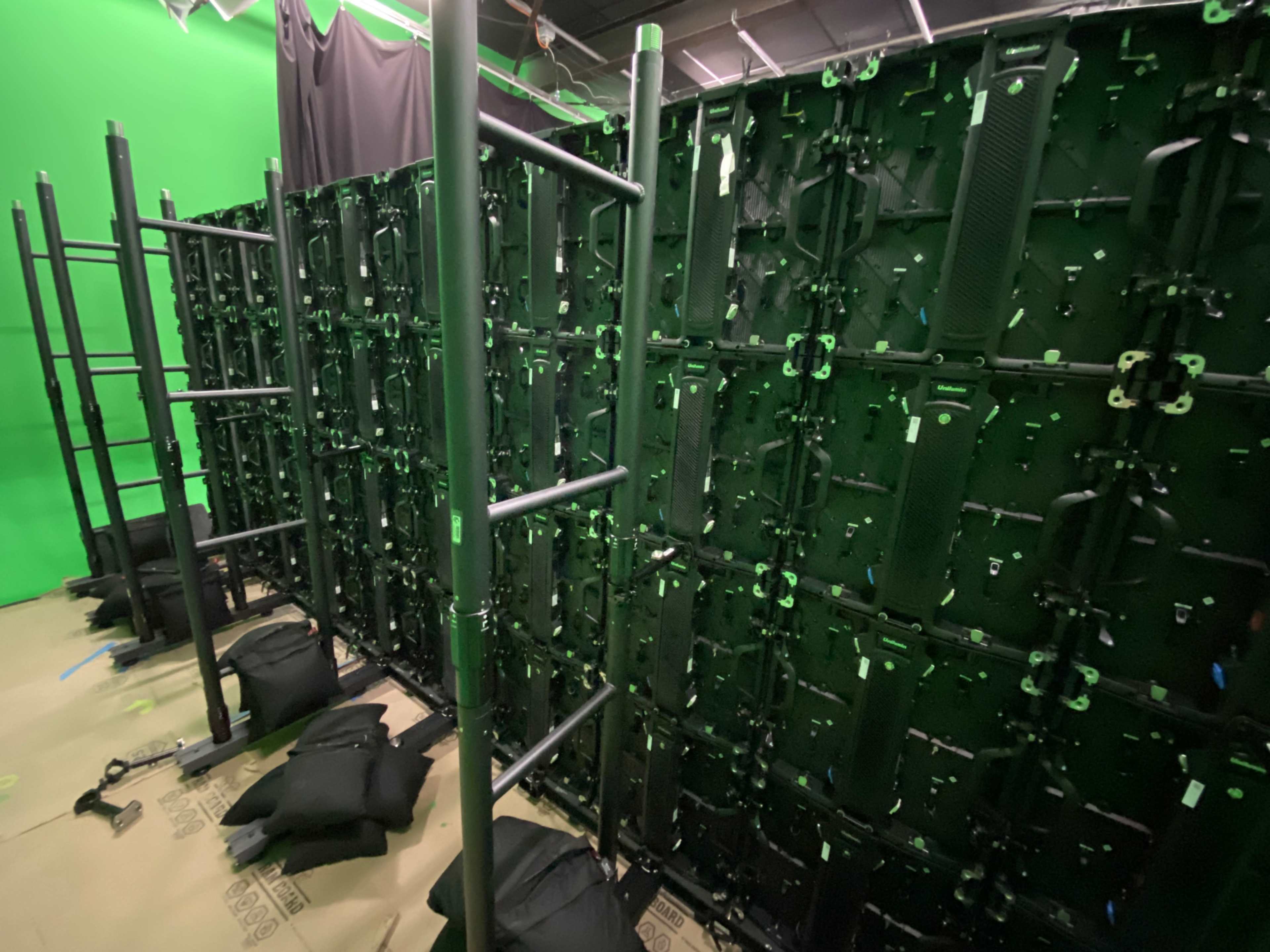 The image shows a green screen setup surrounded by tall, dark structures, likely modular panels used for filming or photography.