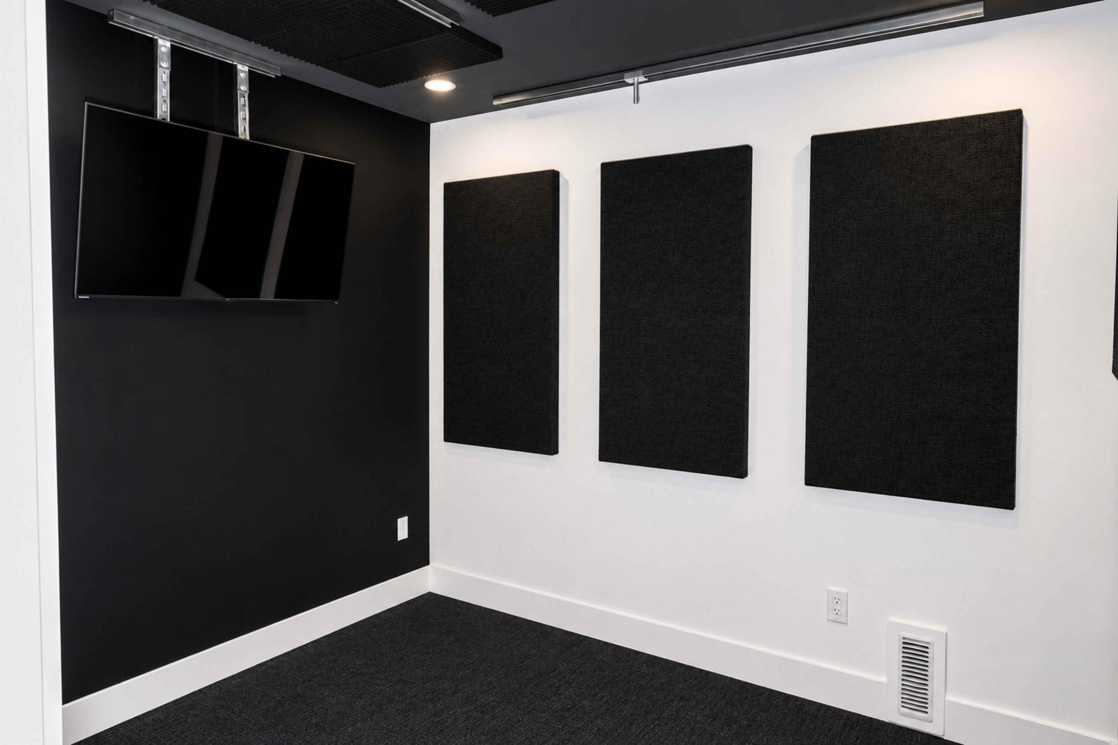 The image shows a modern room with a black and white color scheme, featuring three soundproof panels on the wall and a mounted television.