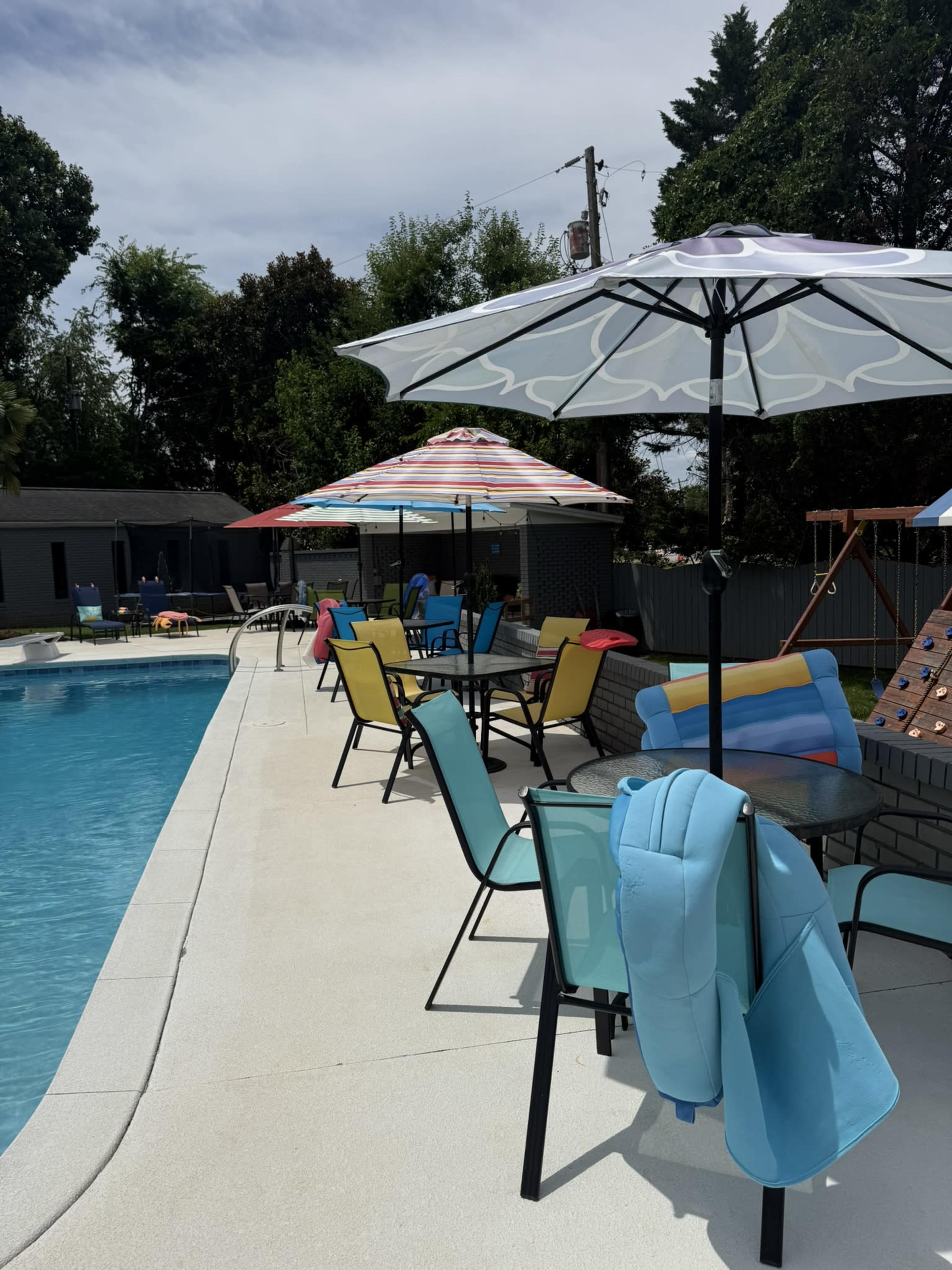 The scene features a swimming pool surrounded by colorful umbrellas and lounge chairs, with a patio area in the background.