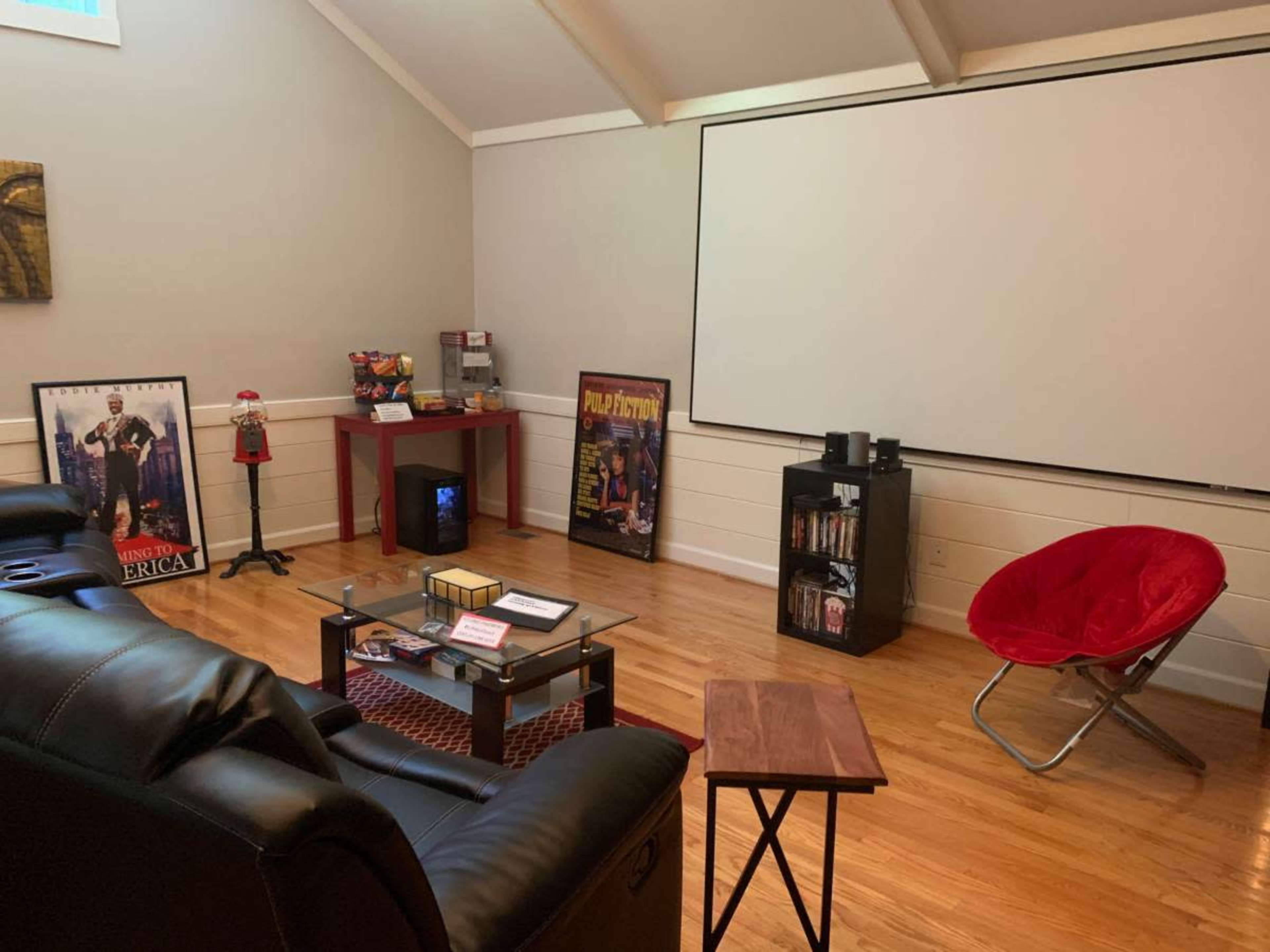 The room features a home theater setup with leather seating, a large projector screen, movie posters, and various entertainment accessories.