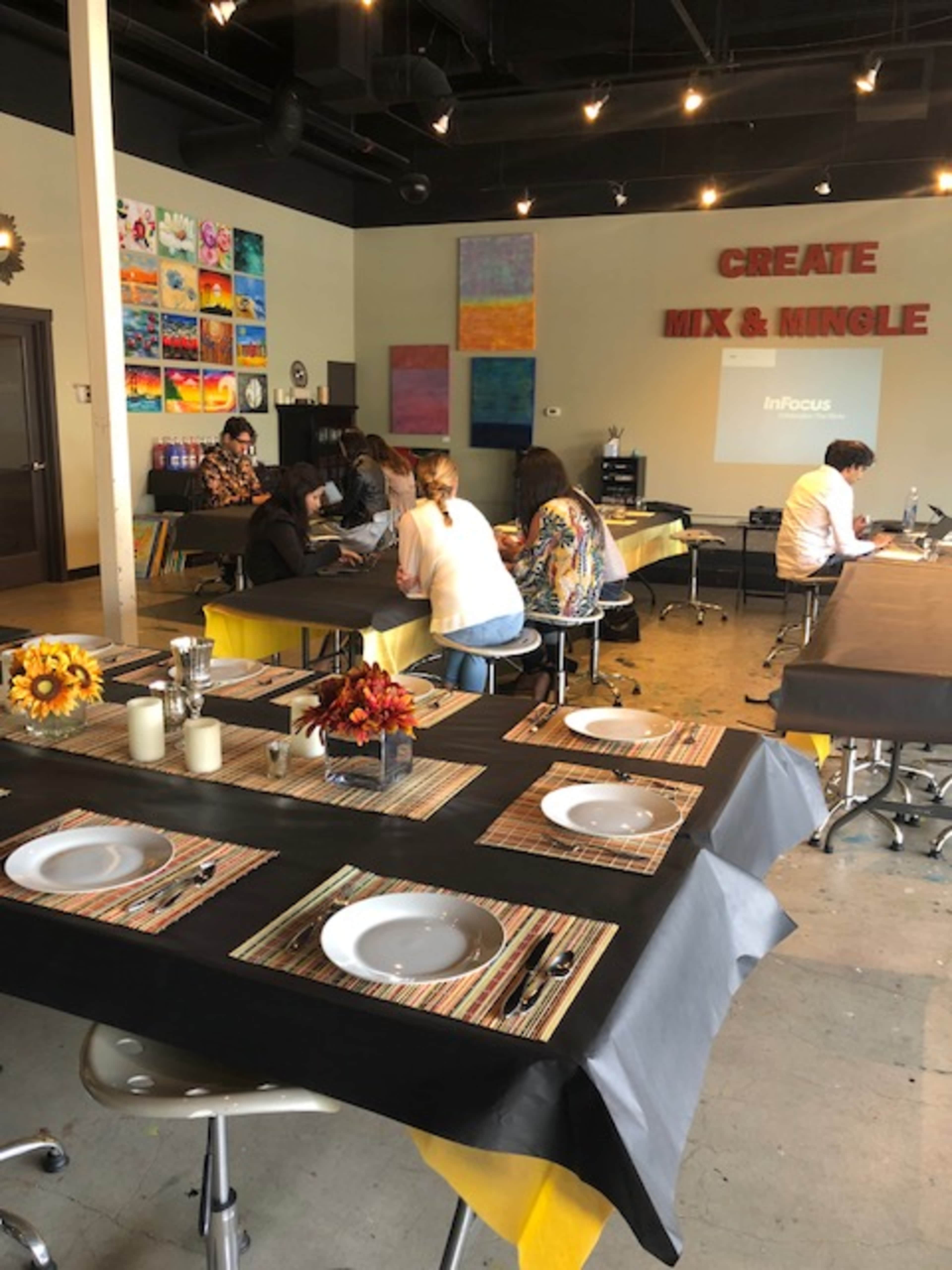 The scene shows a brightly colored art studio set up for a gathering, with tables arranged and decorated for a creative activity.