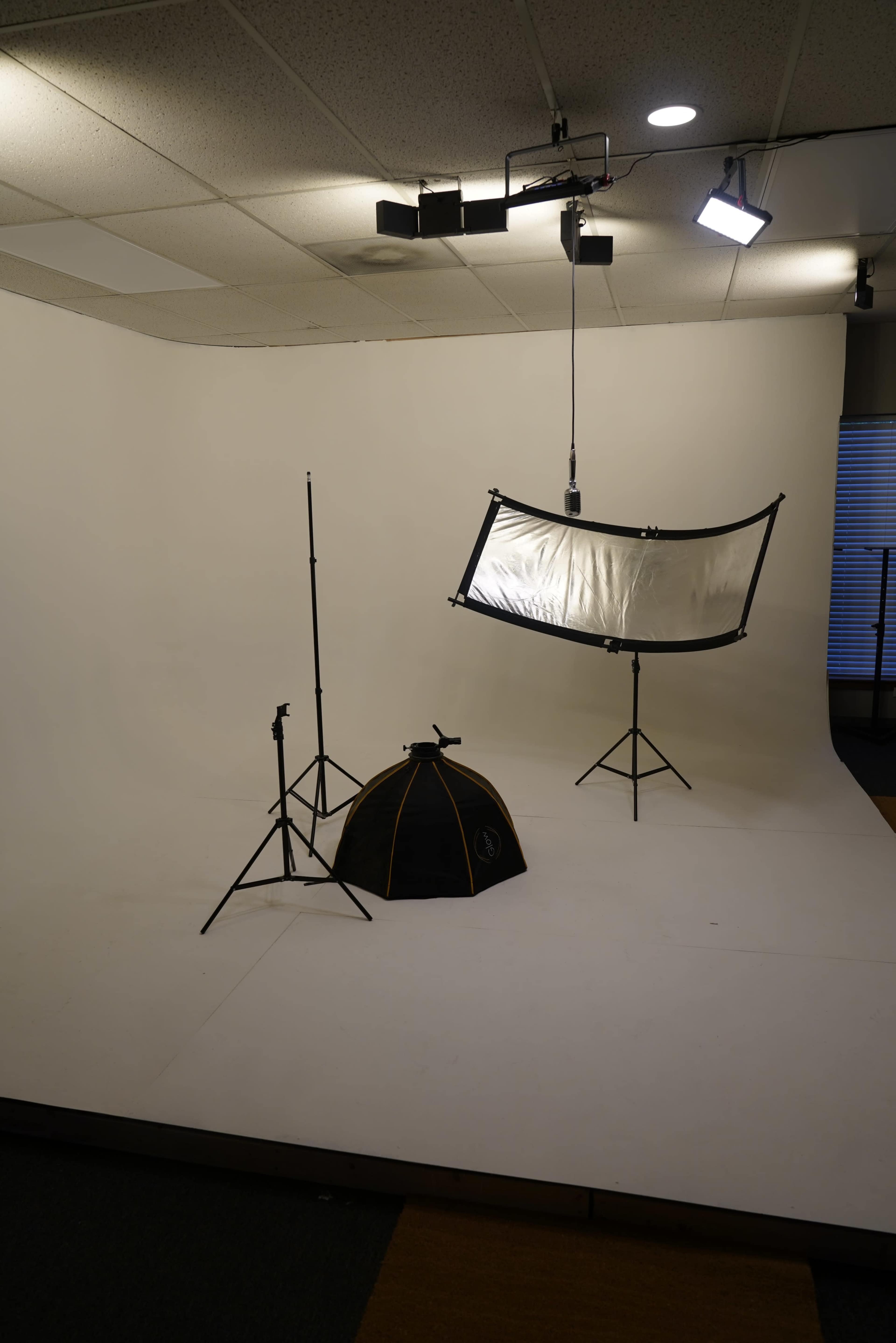 A photography studio setup with a white backdrop, light stands, a black softbox, and a reflector on a stand.