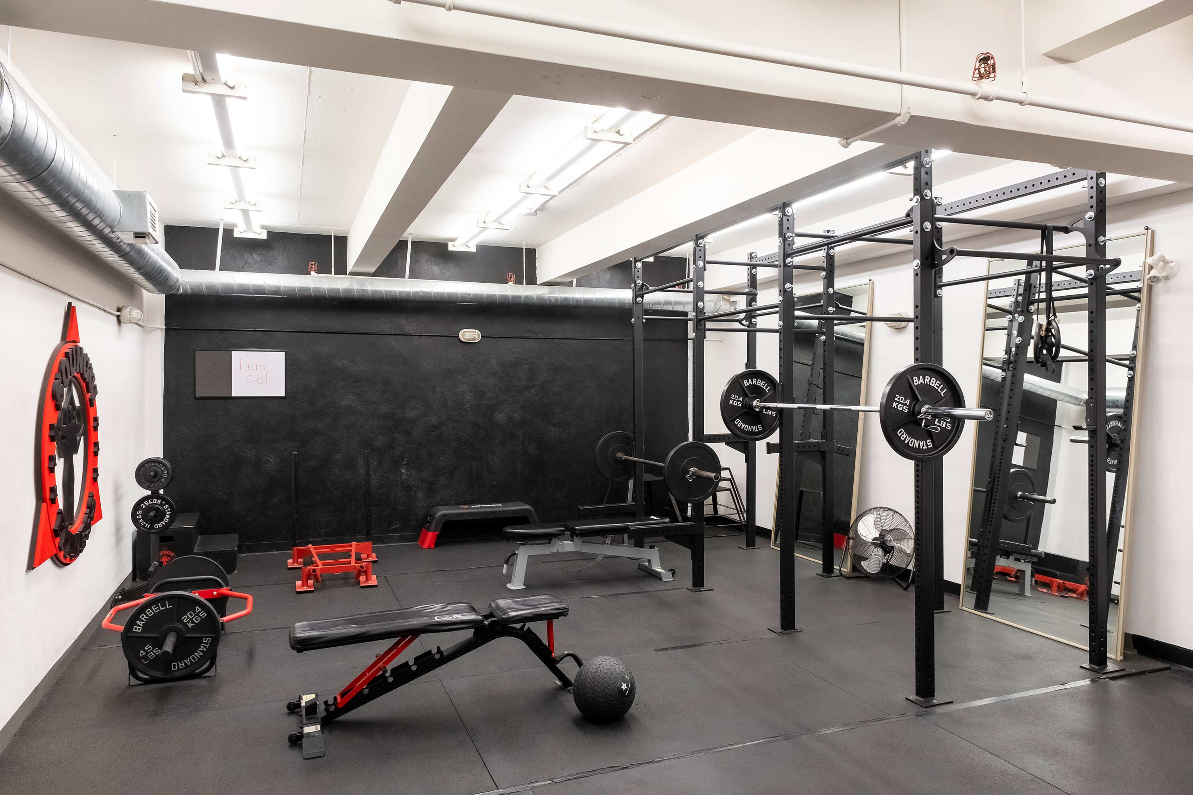 A gym interior featuring various weightlifting equipment, including a squat rack, benches, and free weights on a black rubber floor.