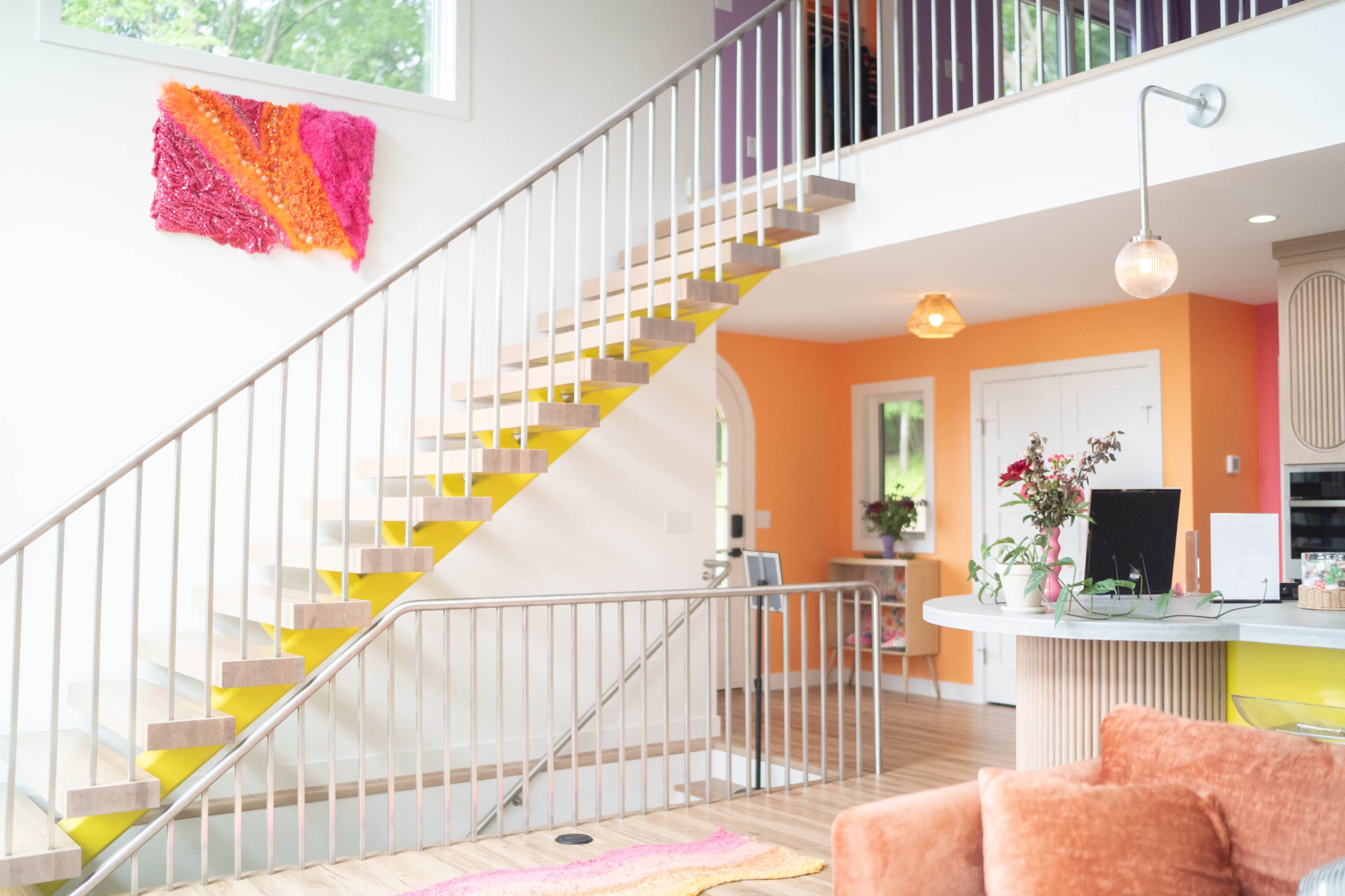 A modern interior features a staircase with colorful steps and a vibrant wall, along with decorative art and a bright living space.