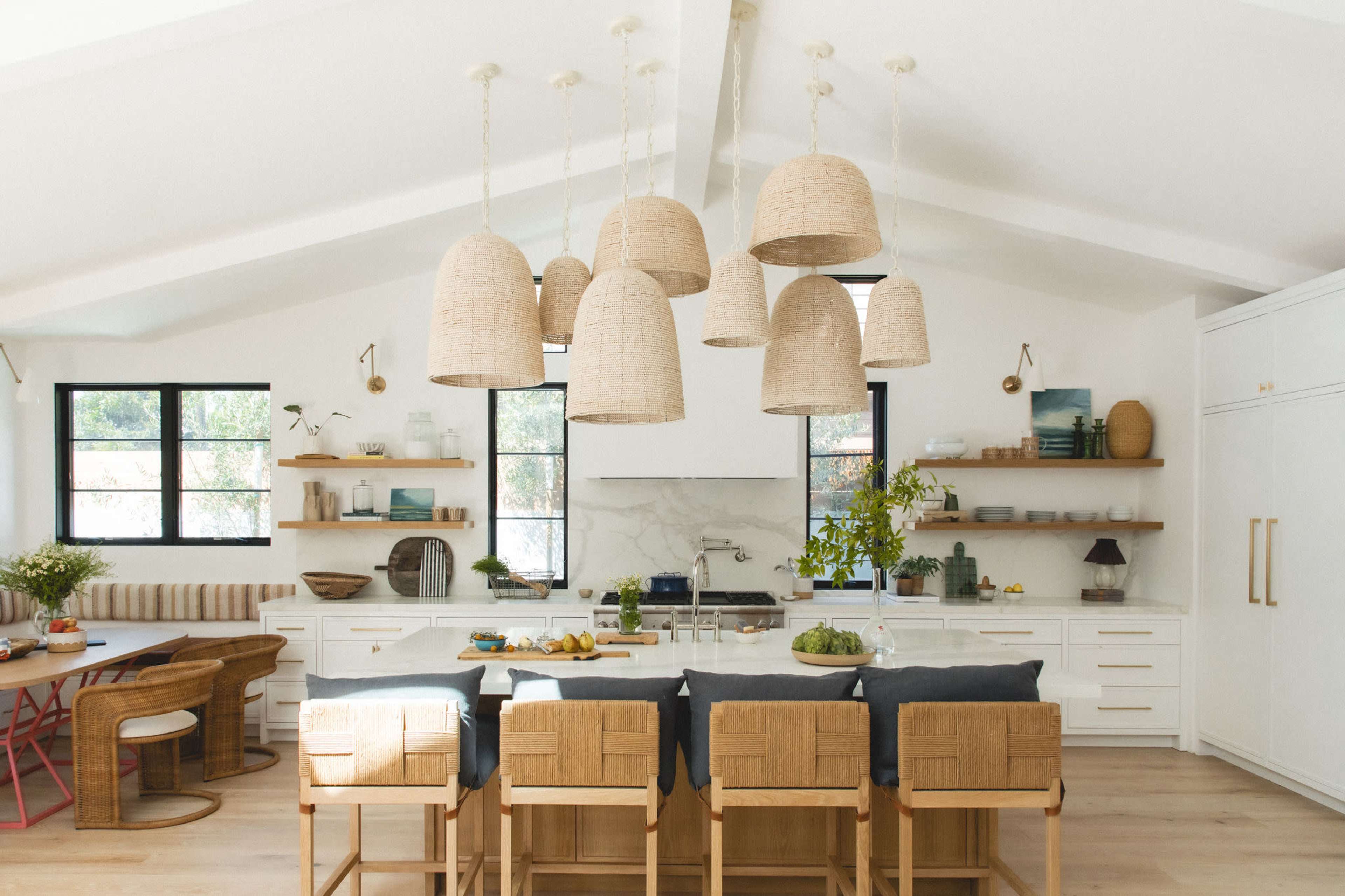 A modern kitchen features a large island with bar seating, pendant lights overhead, and shelves displaying various kitchen items.