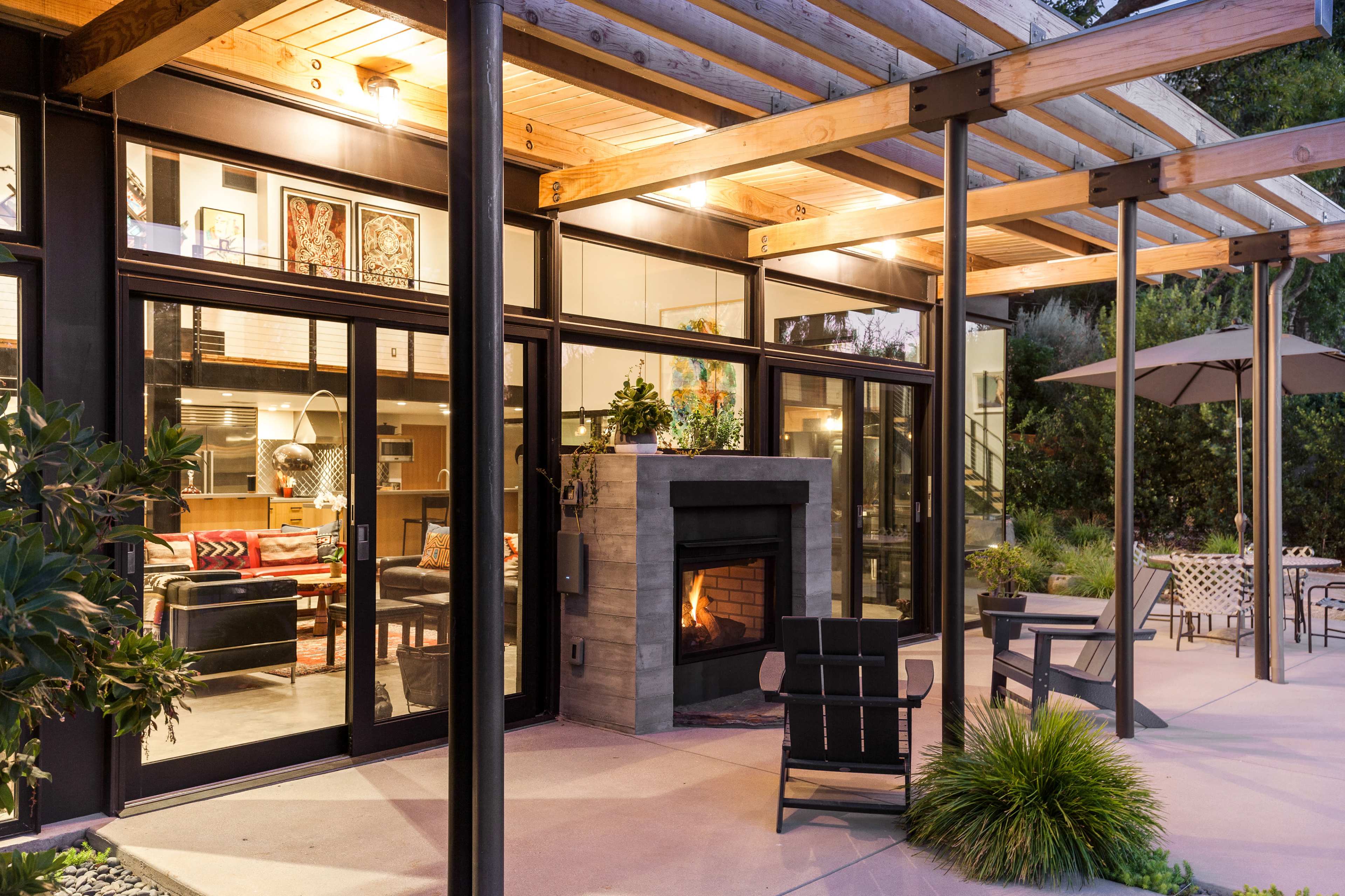 A modern outdoor patio features a fireplace and seating area, with large glass doors leading into a contemporary living space.