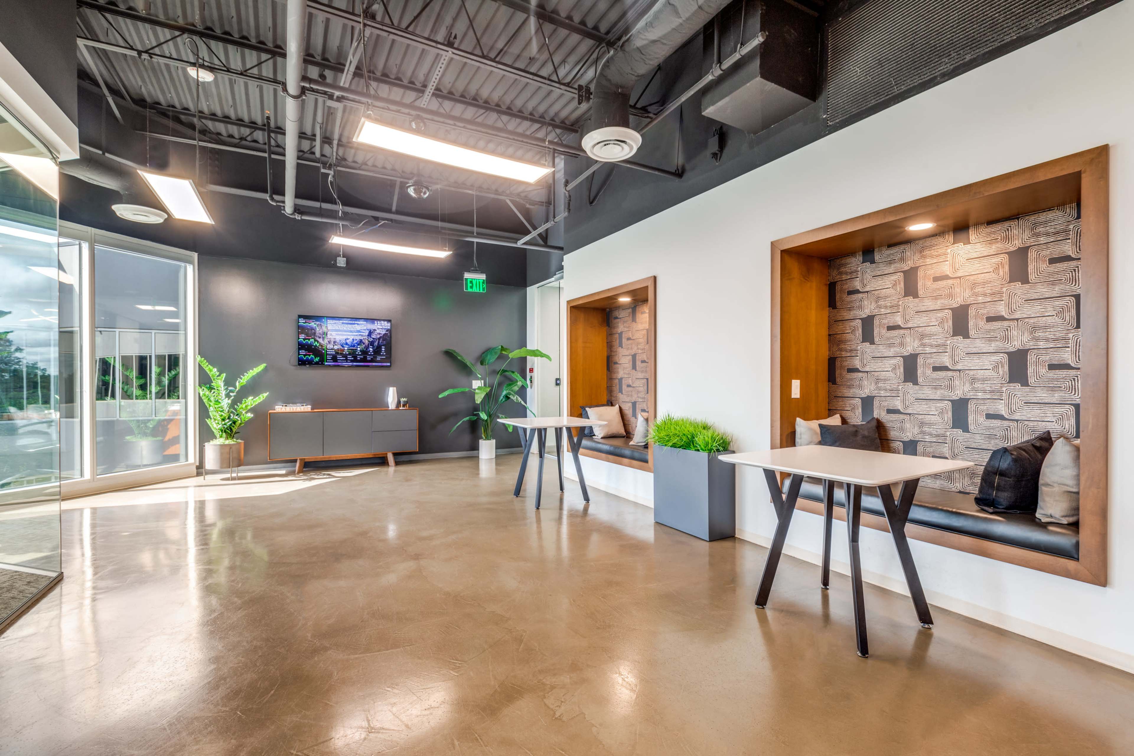 The image shows a modern office lobby with a reception area, two cozy seating nooks, and a television display on the wall.