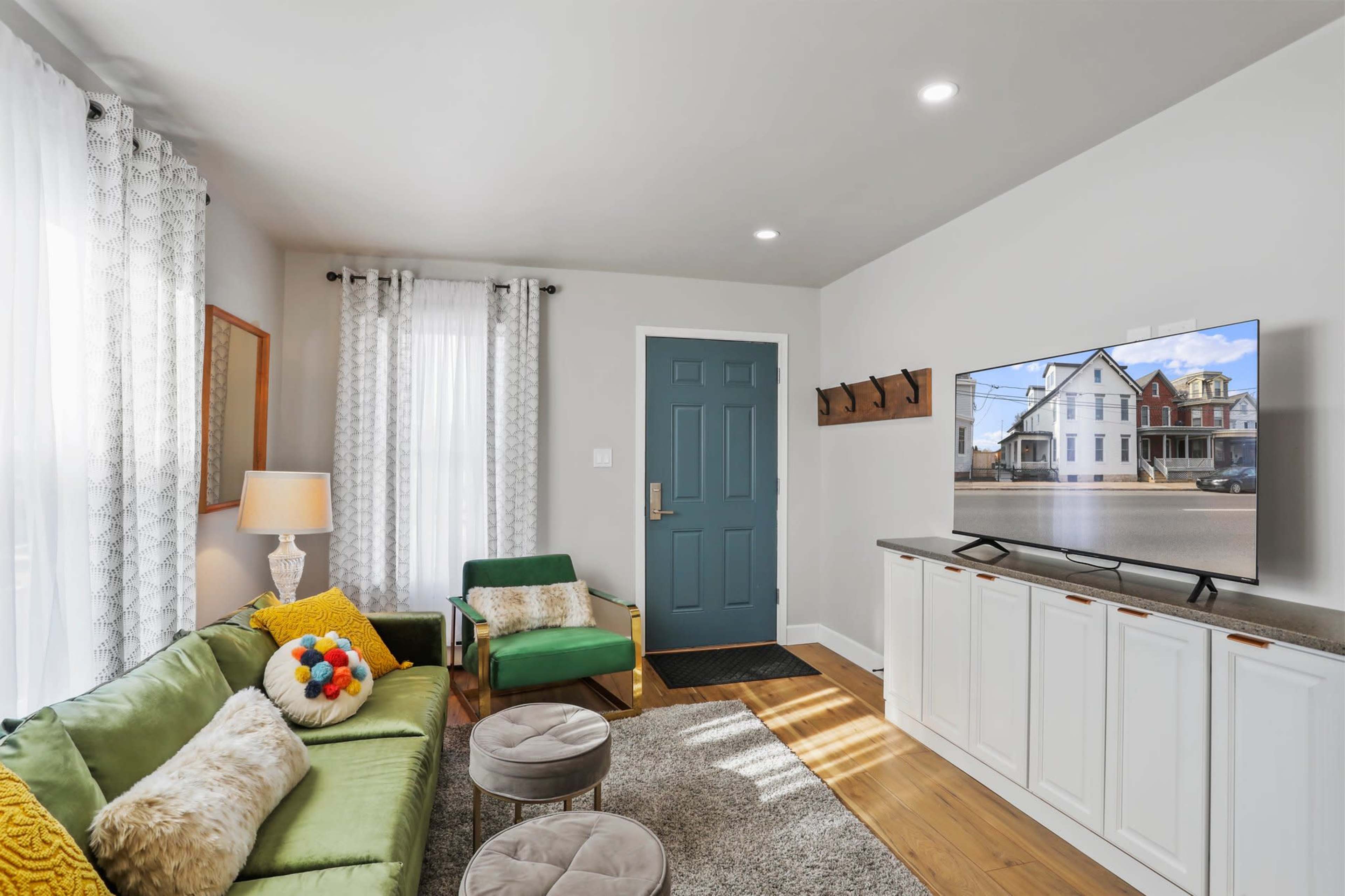 A modern living room with a green sofa, a television mounted on the wall, and a blue front door leading outside.