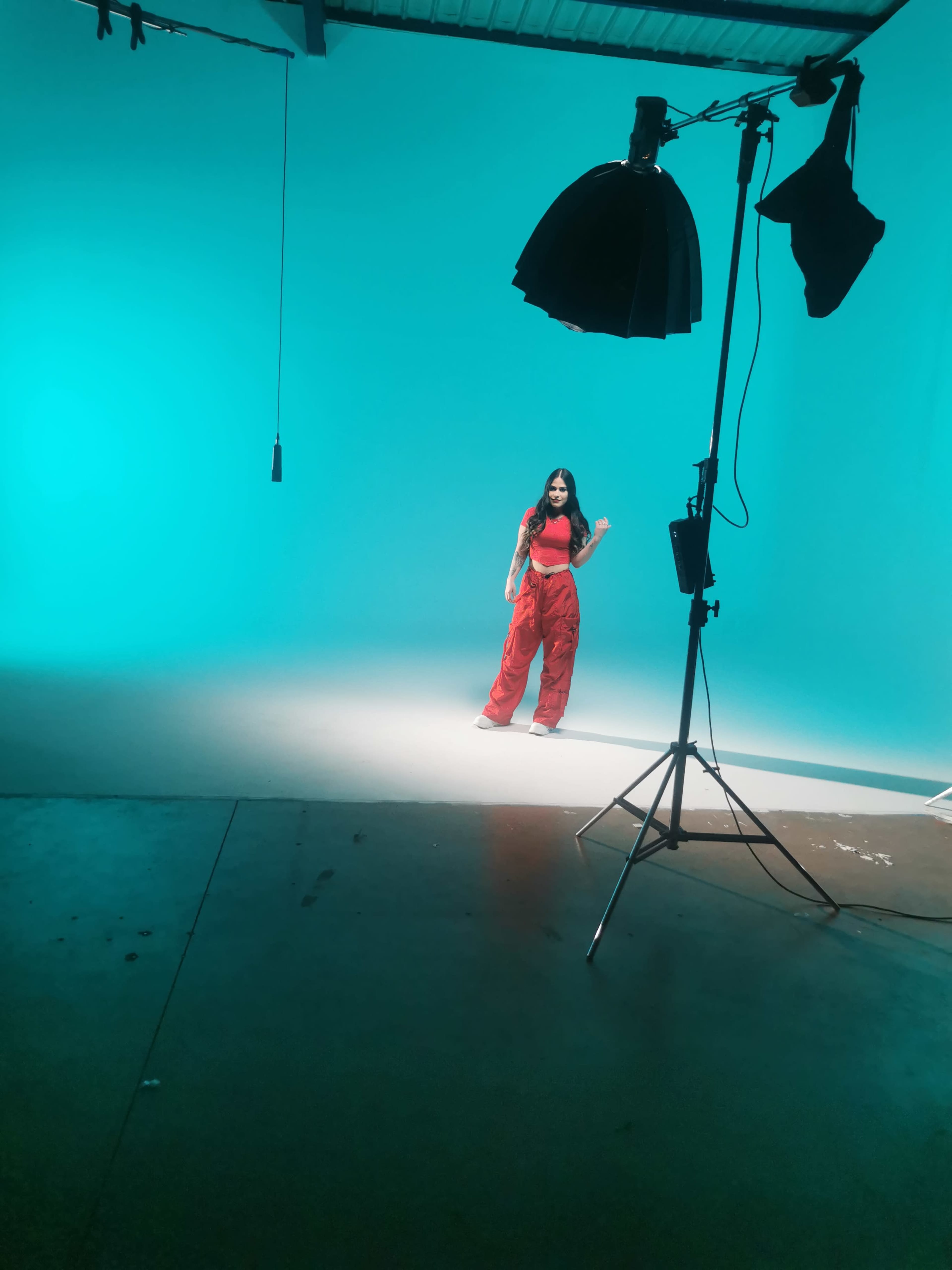 A person poses in a studio with a turquoise backdrop and focused lighting.