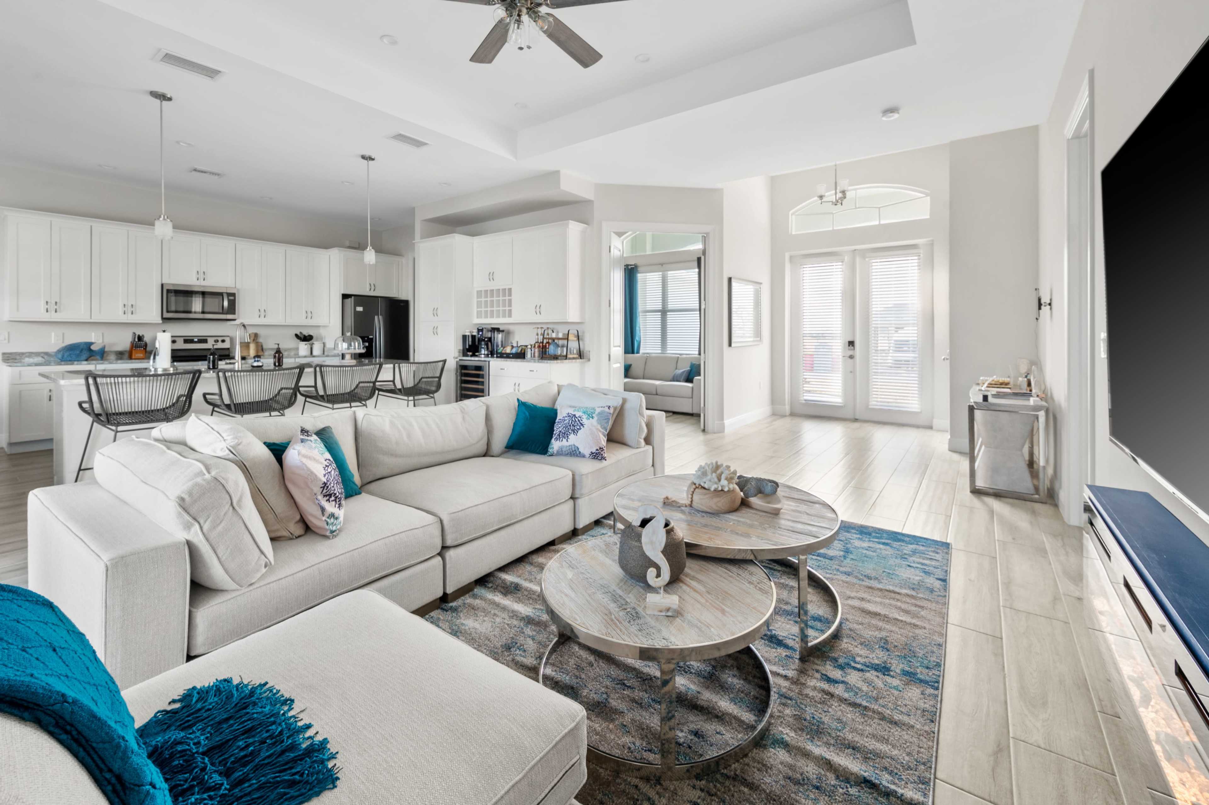 A modern living room with a large sectional sofa, circular wooden coffee tables, and a kitchen area visible in the background.