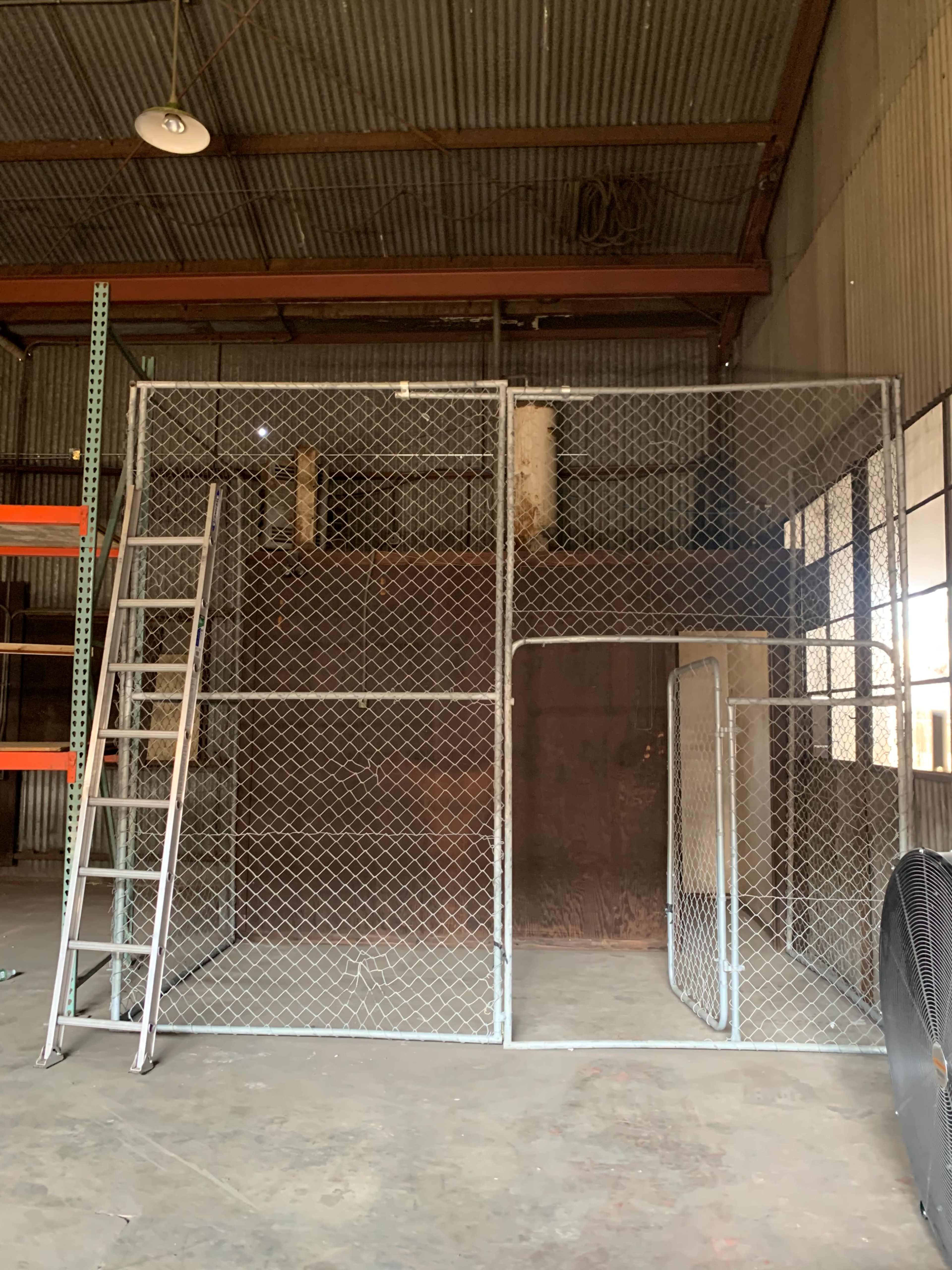 A chain-link fence enclosure with a ladder and a gate inside a warehouse.