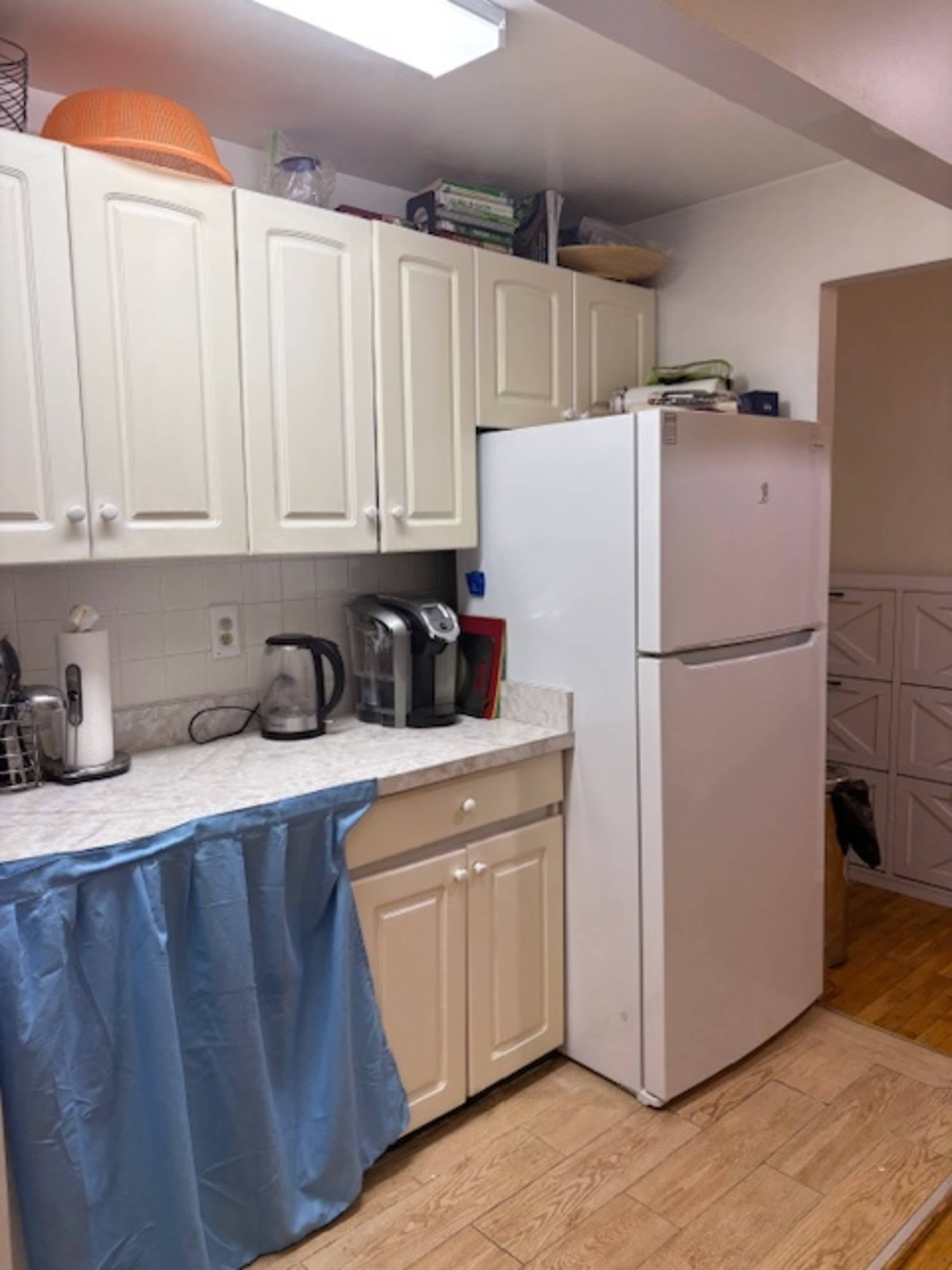 The image shows a kitchen with white cabinets, a countertop, a refrigerator, and various kitchen appliances, including a coffee maker and a kettle.