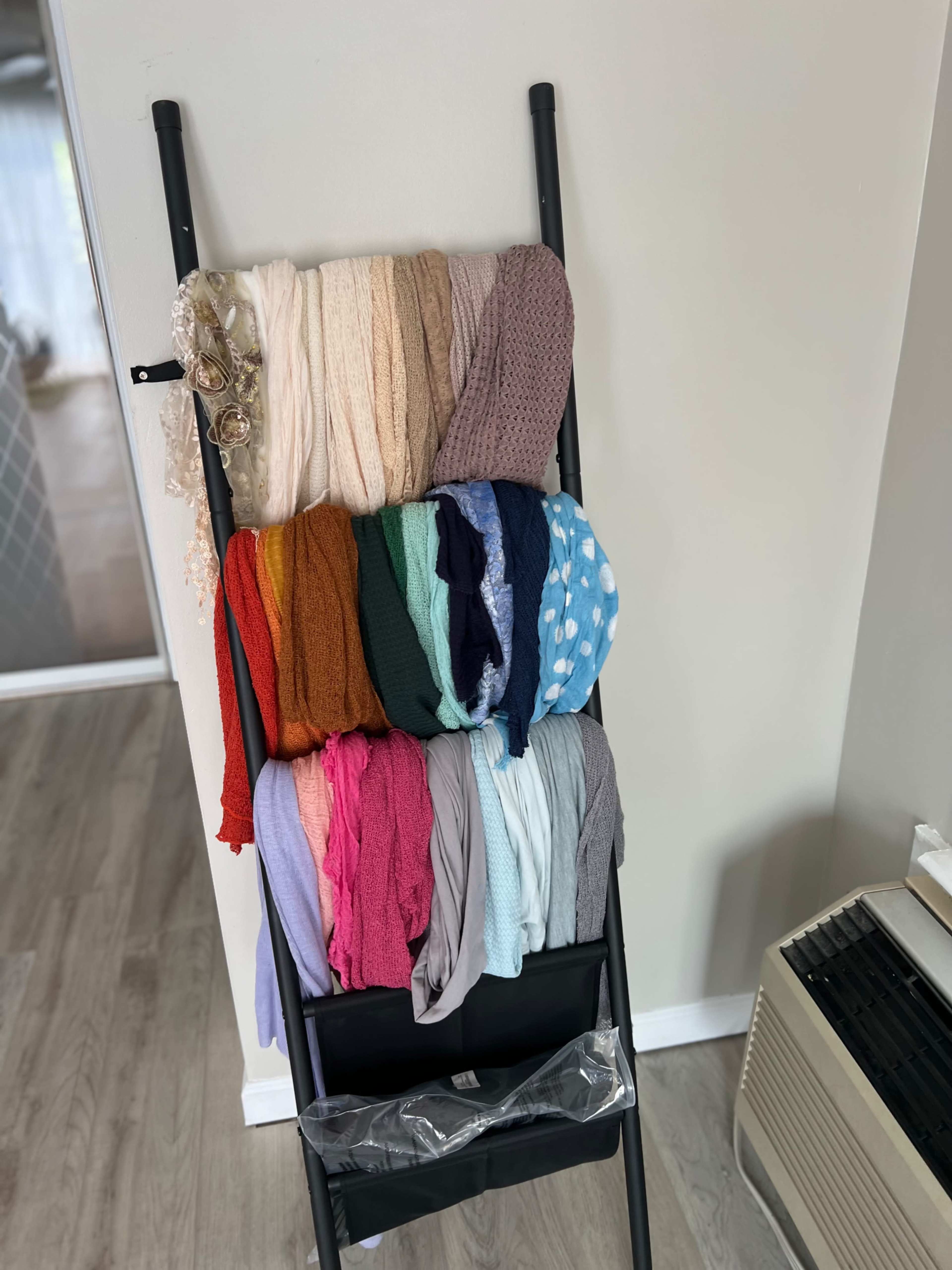 A black rack holds neatly arranged scarves and shawls in various colors and textures.