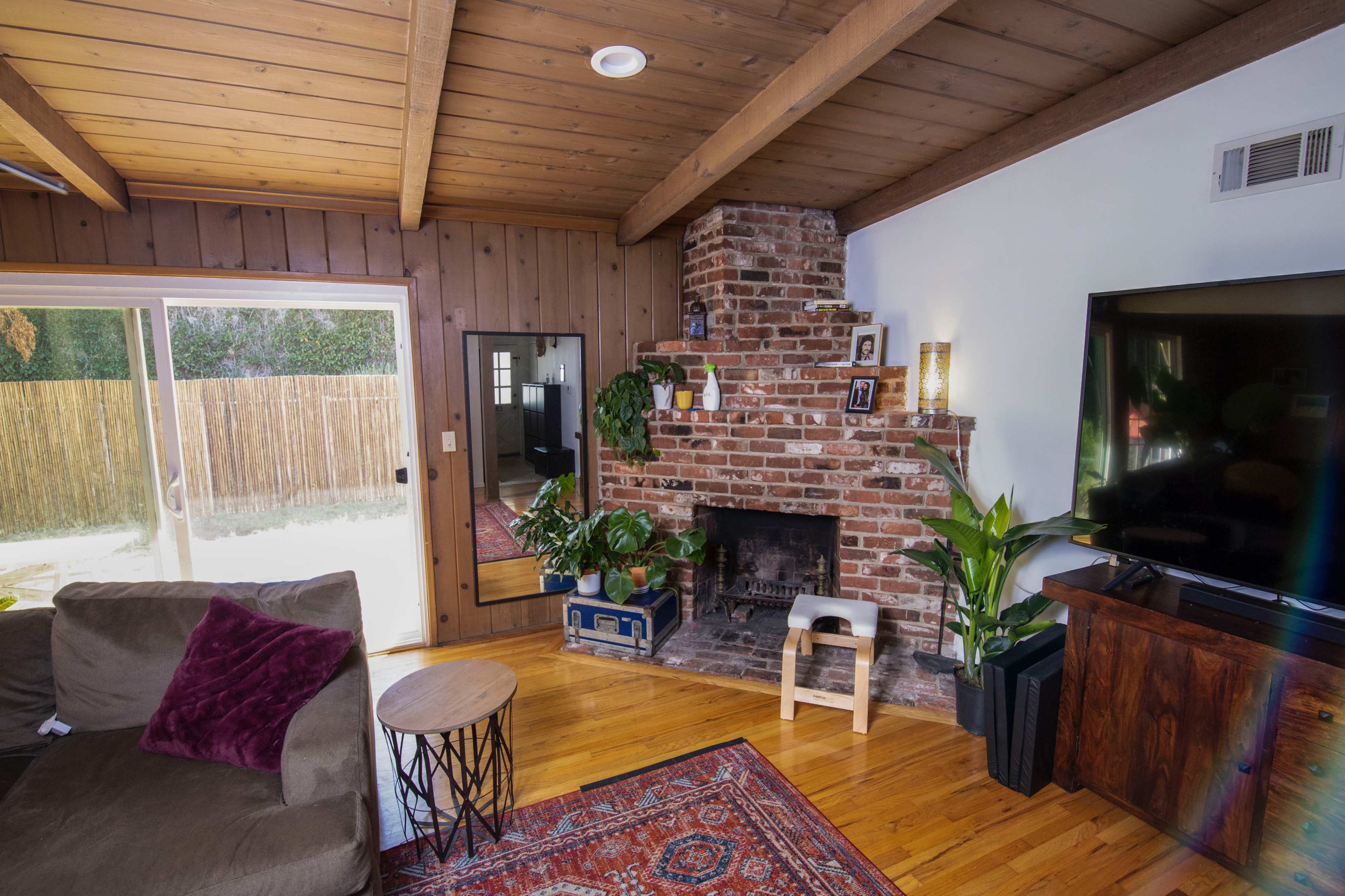 The living room features a brick fireplace, wooden ceiling beams, and a large television opposite a comfortable sofa.