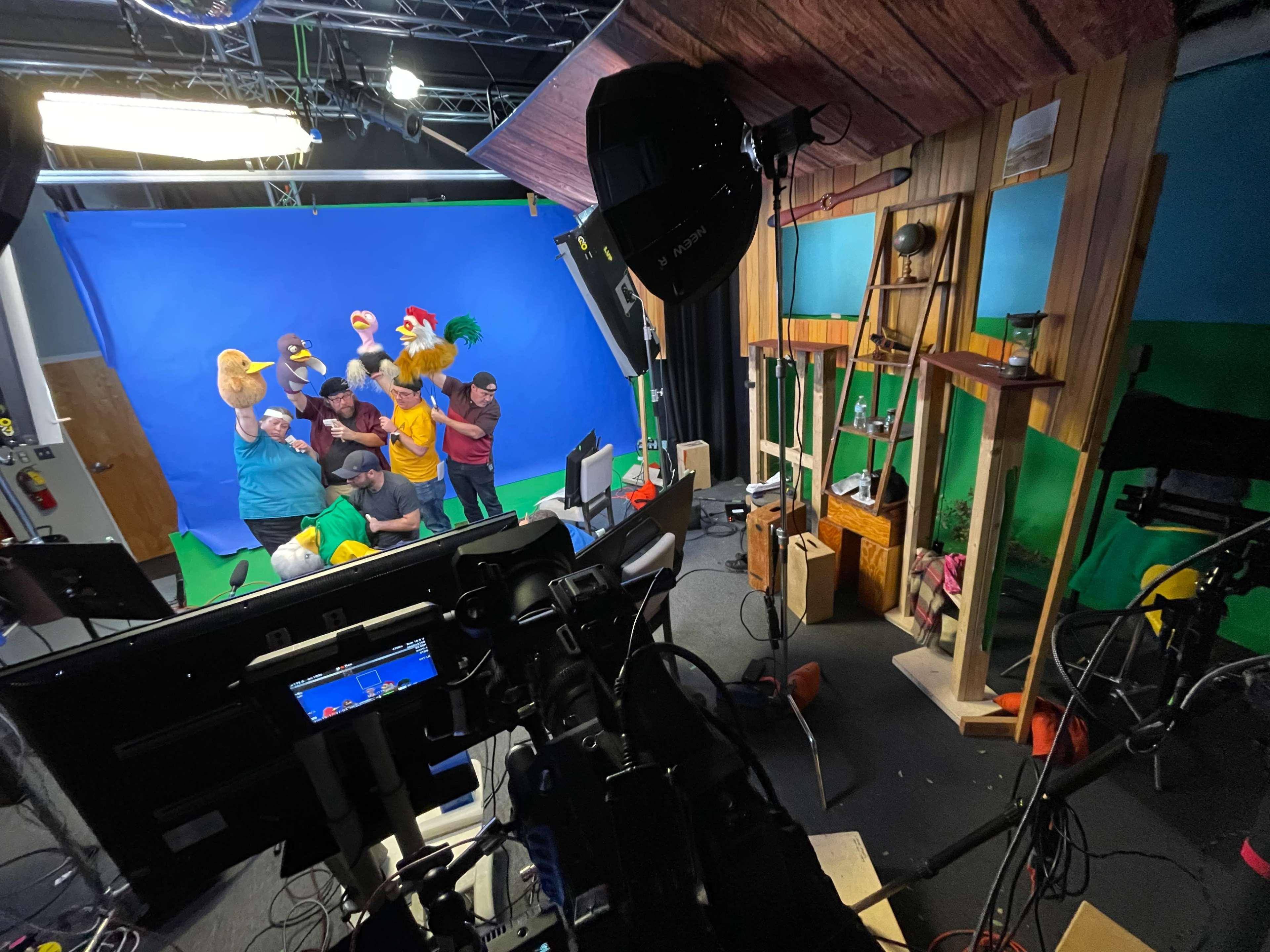 A group of individuals dressed in colorful costumes stands in front of a blue screen, while various cameras and lighting equipment are set up in a studio.